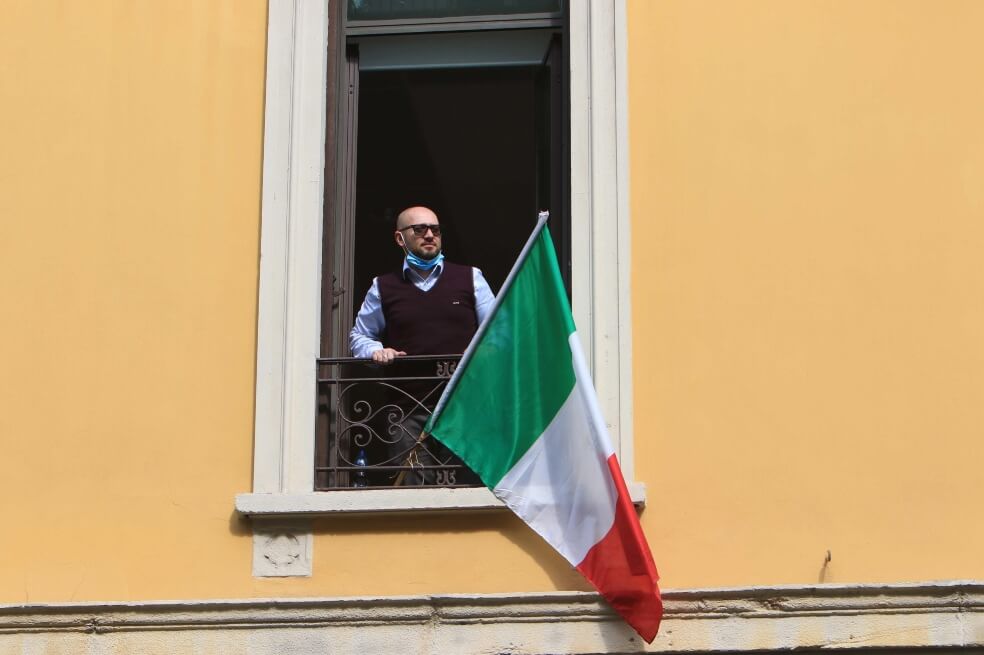 Un ciudadano con la bandera nacional canta en el balcón de su apartamento el himno de Italia. / EFE