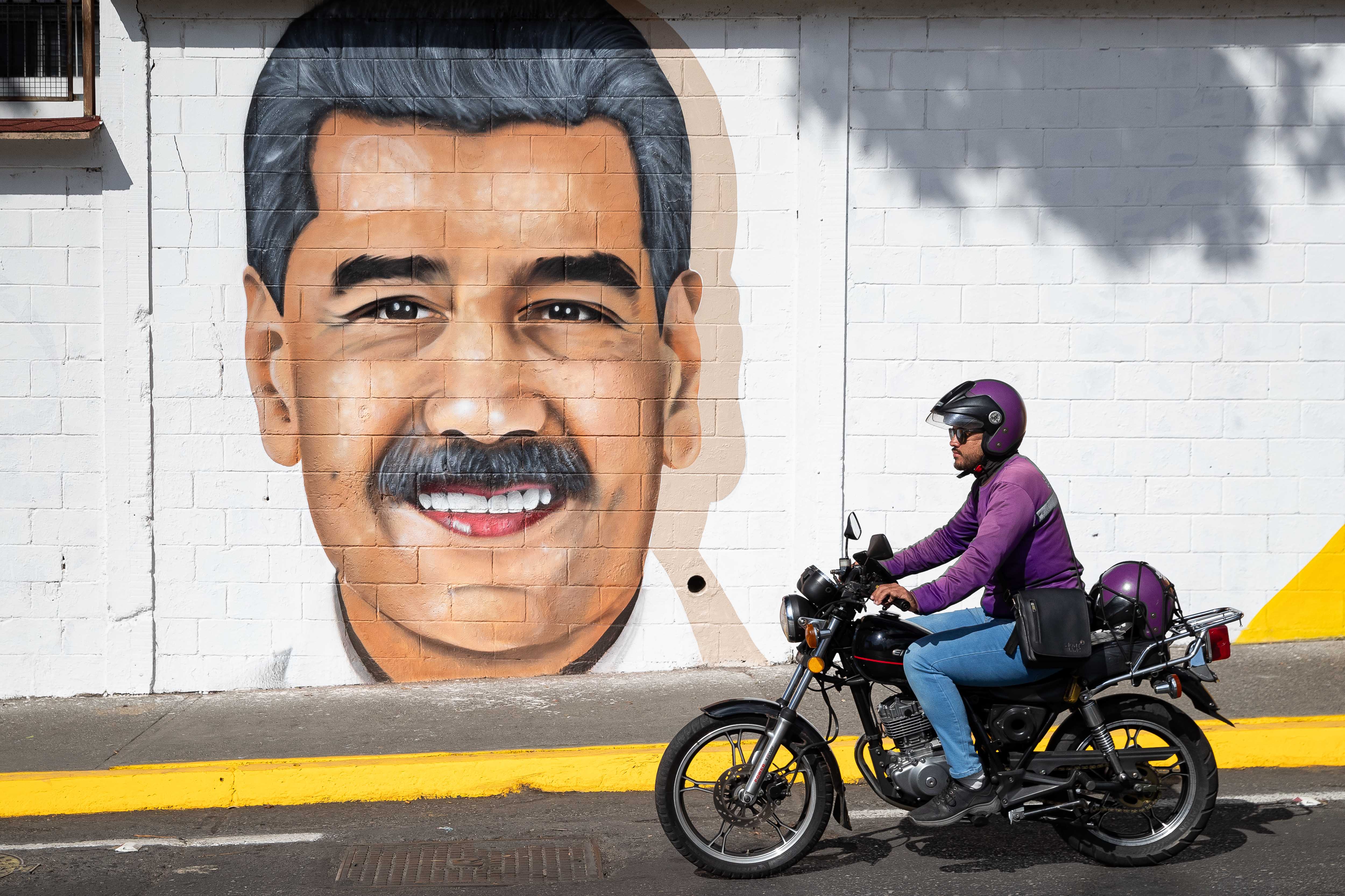 -FOTODELDÍA- AME1315. CARACAS (VENEZUELA), 14/01/2025.- Un motociclista pasa frente a un mural del líder chavista Nicolás Maduro este martes, en Caracas (Venezuela). Venezuela vuelve a una relativa normalidad después de una semana marcada por la escasa actividad comercial y laboral, y las protestas previas a la toma de posesión de la Presidencia, con las calles bajo control del ejército y cuerpos especiales de la Policía. EFE/ Ronald Peña R.