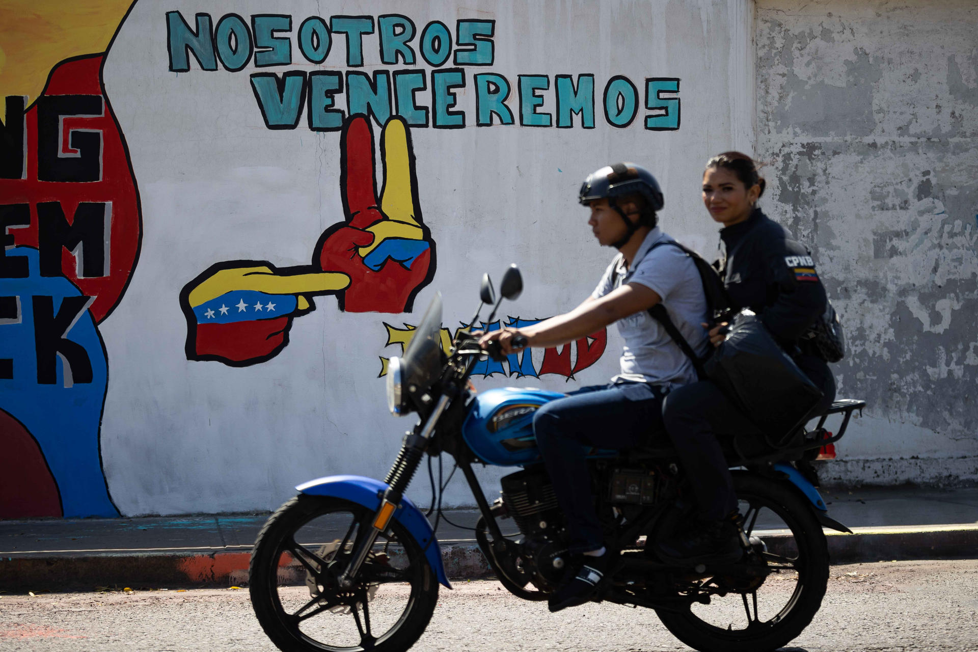 AME9240. CATIA LA MAR (VENEZUELA), 28/01/2026.- Personas en moto transitan frente a un mural del presidente de Venezuela, Nicolás Maduro, este miércoles en Catia La Mar (Venezuela). EFE/Ronald Peña R
