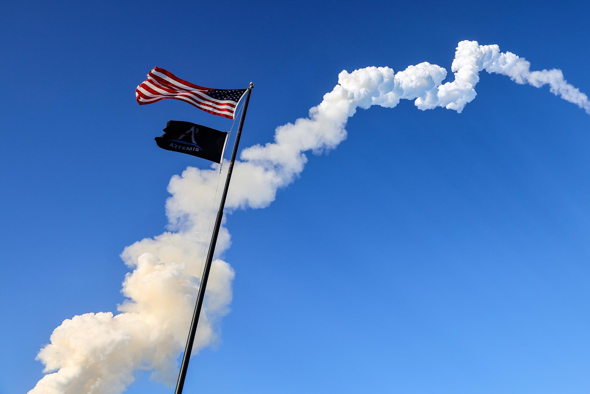 TITUSVILLE (United States), 02/04/2026.- The US flag flutters in the wind as the trail of the Space Launch System (SLS) rocket carrying the Orion capsule for the Artemis II mission crosses the sky after launch from Launch Pad 39B at the Kennedy Space Center in Titusville, Florida, USA, 01 April 2026. The crew includes NASA astronauts Reid Wiseman, commander, Victor Glover, pilot, Christina Koch, mission specialist, and Canadian Space Agency (CSA) astronaut Jeremy Hansen, mission specialist. The mission will conduct a crewed flyby of the Moon, the first human flight beyond low Earth orbit since 1972. EFE/EPA/CRISTOBAL HERRERA-ULASHKEVICH