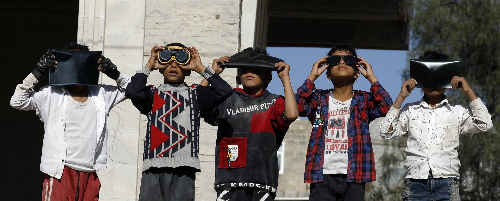Los niños usan gafas protectoras y placas de rayos X para observar un eclipse solar parcial en Sana'a, Yemen.