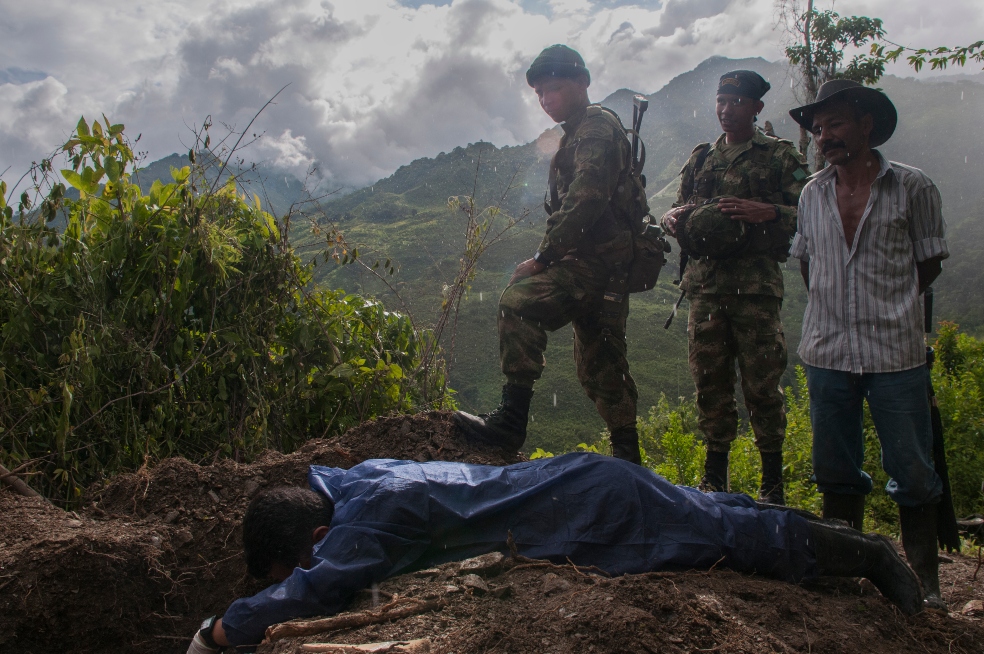 Cuatro hombres miran hacia un hueco en la tierra donde hay restos óseos. Uno de ellos está intentando sacarlos.