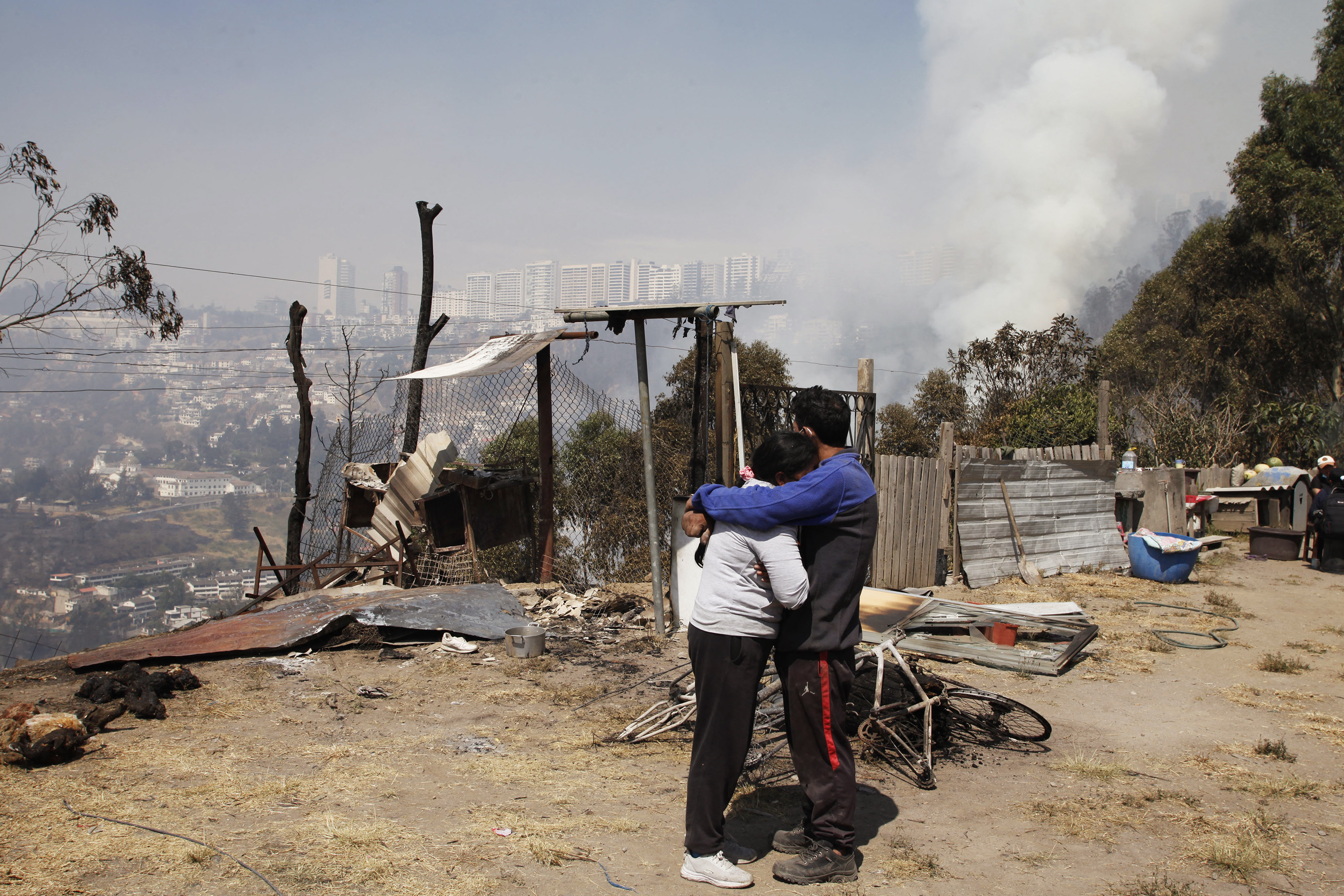 Muchos ecuatorianos no quieren dejar sus casas por miedo a sufrir algún tipo de criminalidad. En la imagen, una pareja se abraza mientras el humo se eleva desde un incendio forestal en una colina.