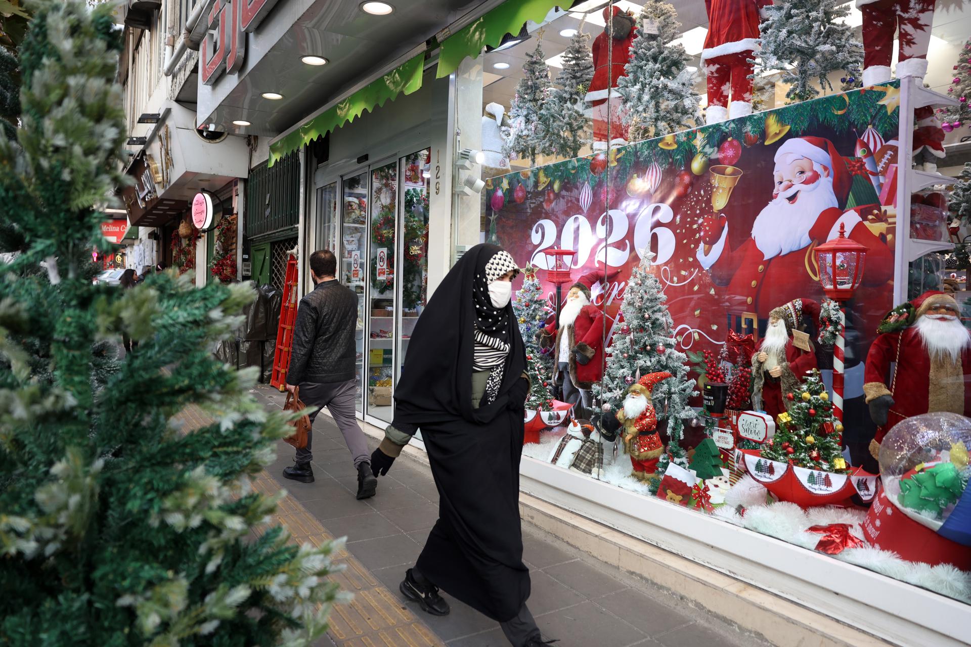 TEHRAN (IRAN(Islamic Republic Of)), 23/12/2025.- A veiled Iranian woman walk pasts a shop selling Christmas items in Tehran, Iran, 23 December 2025. Approximately 150,000 Christians live in Iran, with Armenians constituting the majority. They celebrate Christmas in churches and privately at home. Some Muslim families have also adopted a few Christmas traditions, buying presents and even Christmas trees for their children to enjoy. (Teherán) EFE/EPA/ABEDIN TAHERKENAREH