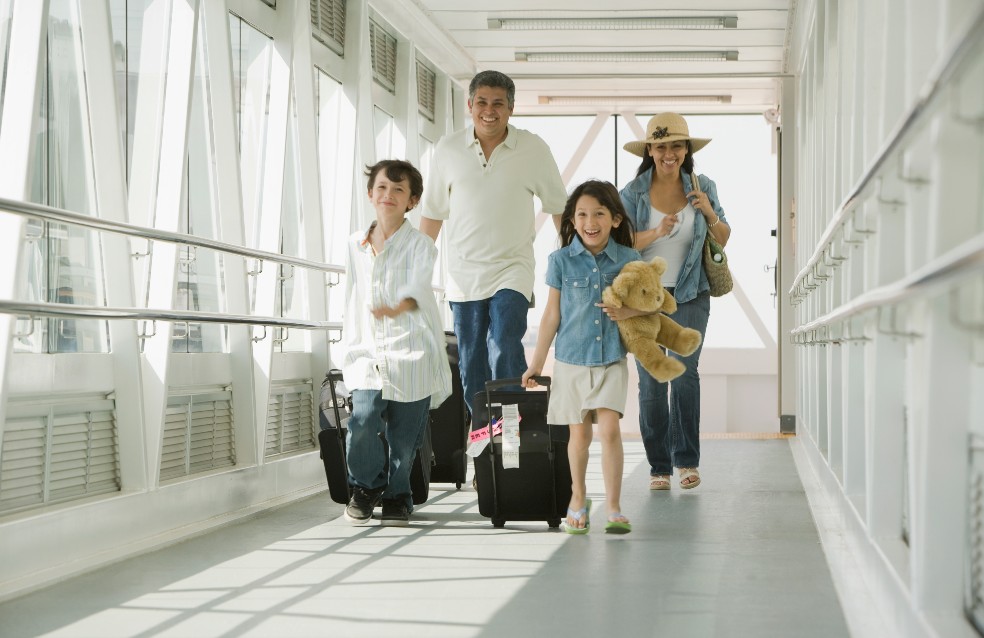 Papá y mamá, con sus dos hijos menores de edad, corren por el pasillo de un aeropuerto arrastrando sus maletas.