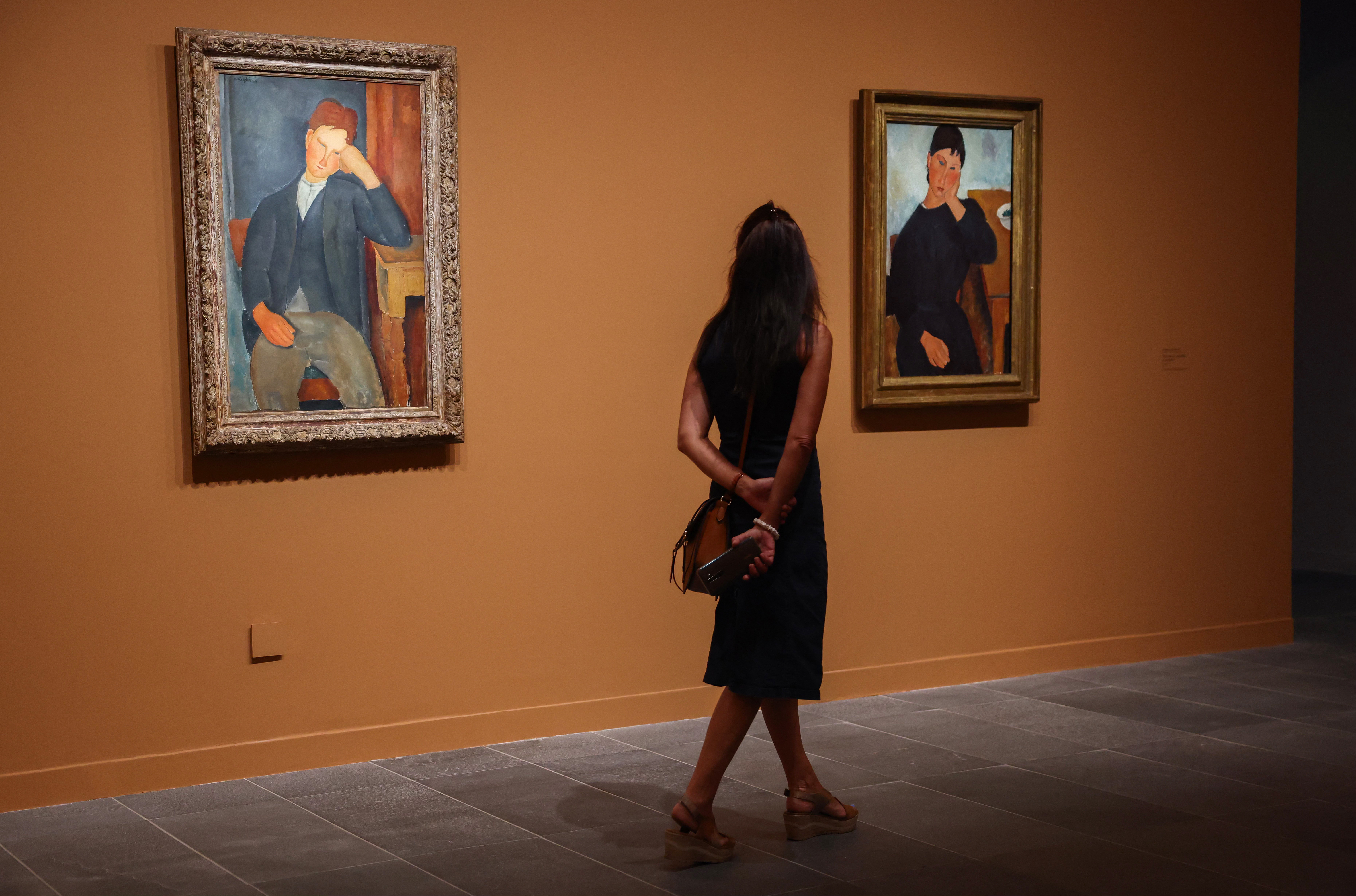 Un visitante se encuentra entre los óleos "El joven aprendiz" (1918-1919) y "Elvira descansando en una mesa" (1919) del pintor italiano Amadeo Modigliani (1884-1920) en el museo de la Orangerie de París el 15 de septiembre de 2023. en el marco de la exposición "Amadeo Modigliani, un pintor y su marchante".