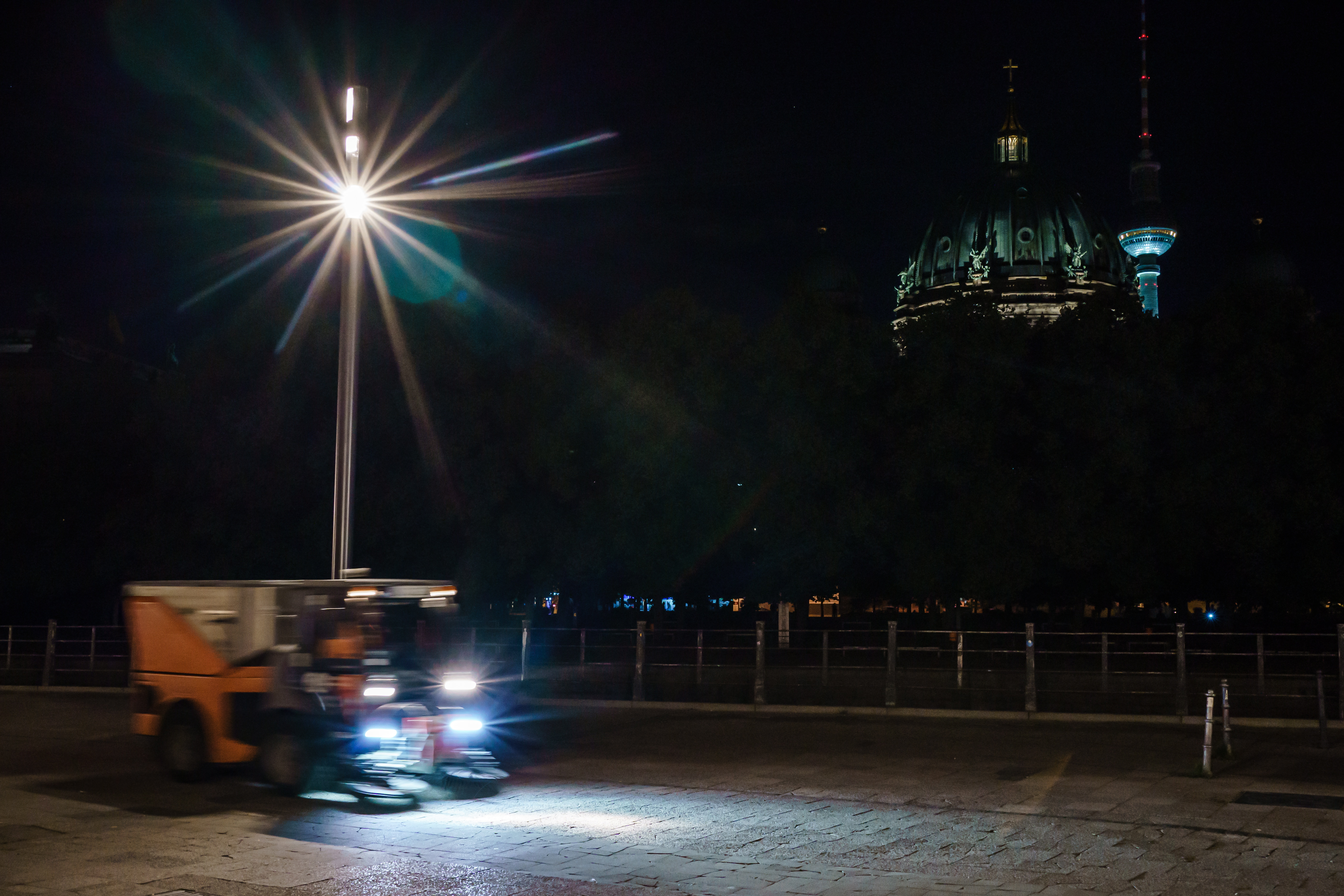 Una persona limpia el pavimento mientras la cúpula de la Catedral de Berlín 'Berliner Dom' (izq.) muestra solo unos pocos signos de iluminación junto a la torre de televisión de Berlín (der.).