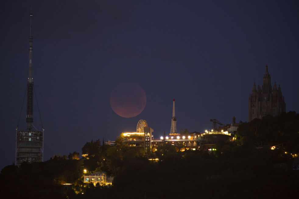 Vista del eclipse total de Luna tras el parque de atracciones del Tibidabo, en España.