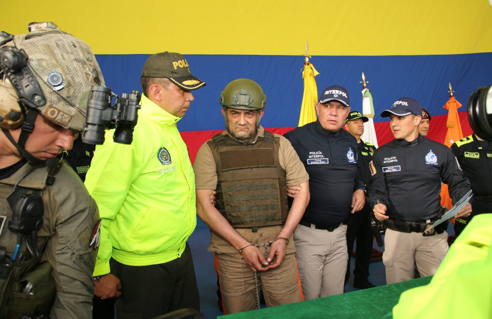 AME6953. BOGOTÁ (COLOMBIA), 05/05/2022.- Fotografía cedida hoy por la Policía Nacional de Colombia que muestra al capturado jefe del Clan del Golfo, Dairo Antonio Úsuga David, alias Otoniel (c), durante su extradición a EE.UU el 4 de mayo de 2022 en Bogotá (Colombia). El jefe de la banda criminal Clan del Golfo, alias Otoniel, comparecerá este jueves ante una jueza en Nueva York, un día después de haber sido extraditado a Estados Unidos desde Colombia. La Fiscalía Federal del distrito este de Nueva York confirmó a Efe que Otoniel se presentará ante la jueza federal Vera Scanlon a las 15.00 hora local (19.00 GMT). EFE/ Policia Nacional de Colombia /SOLO USO EDITORIAL /SOLO DISPONIBLE PARA ILUSTRAR LA NOTICIA QUE ACOMPAÑA (CRÉDITO OBLIGATORIO)