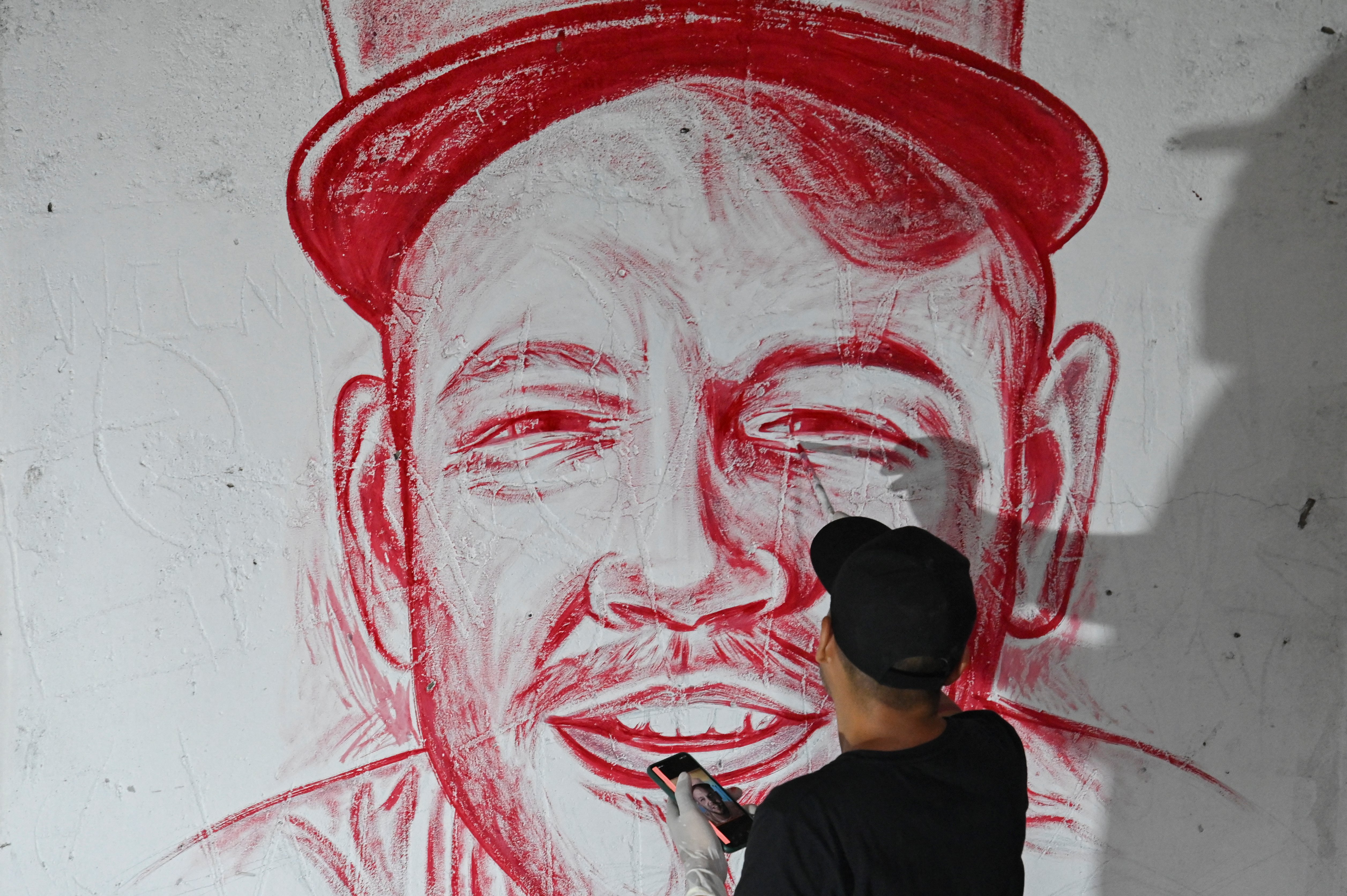 El artista colombiano Julián Castillo pinta con sangre humana un mural del cantante puertorriqueño  René Pérez, Residente, en el barrio Siloé en Cali, el 23 de marzo de 2022, en rechazo a la violencia. 
(Foto por Luis ROBAYO / AFP)