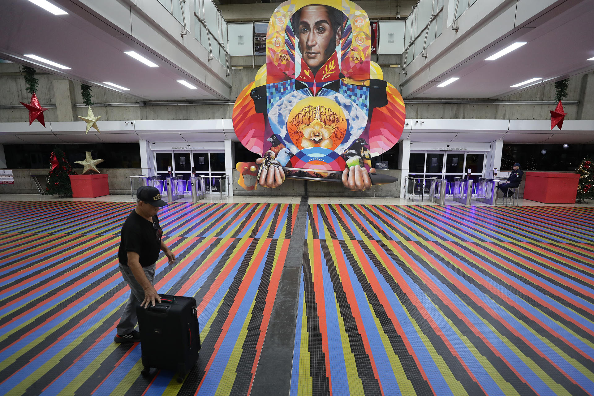 FOTODELDÍA AME2994. MAIQUETIA (VENEZUELA), 26/11/2025.- Una persona camina frente a una imagen del héroe latinoamericano Simón Bolívar este miércoles, en el aeropuerto internacional Simón Bolívar, que sirve a Caracas, en Maiquetía (Venezuela). El plazo de 48 horas que otorgó el Gobierno de Venezuela a las aerolíneas para que retomen sus operaciones en el país suramericano terminó sin que hasta el momento las autoridades hayan confirmado su decisión de revocar los permisos de "vuelo permanente" o hayan anunciado algún otro tipo de sanción. EFE/ Ronald Pena R
