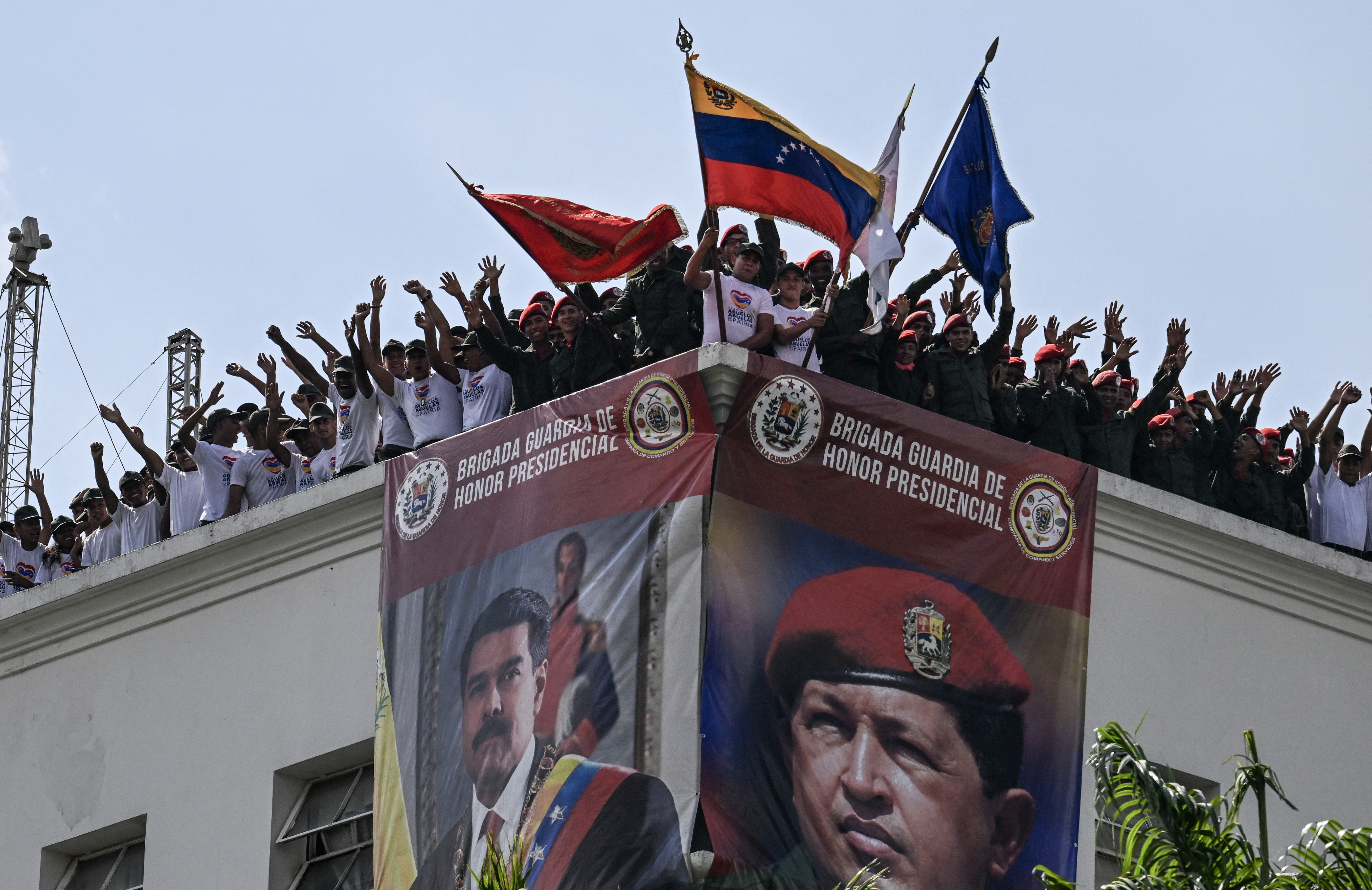 (FILES) Members of the Presidential Honor Guard display a Venezuelan national flag on a terrace of the Miraflores Presidential Palace decorated with images of President Nicolas Maduro (L) and late President Hugo Chavez during a rally in Caracas on May 17, 2024.