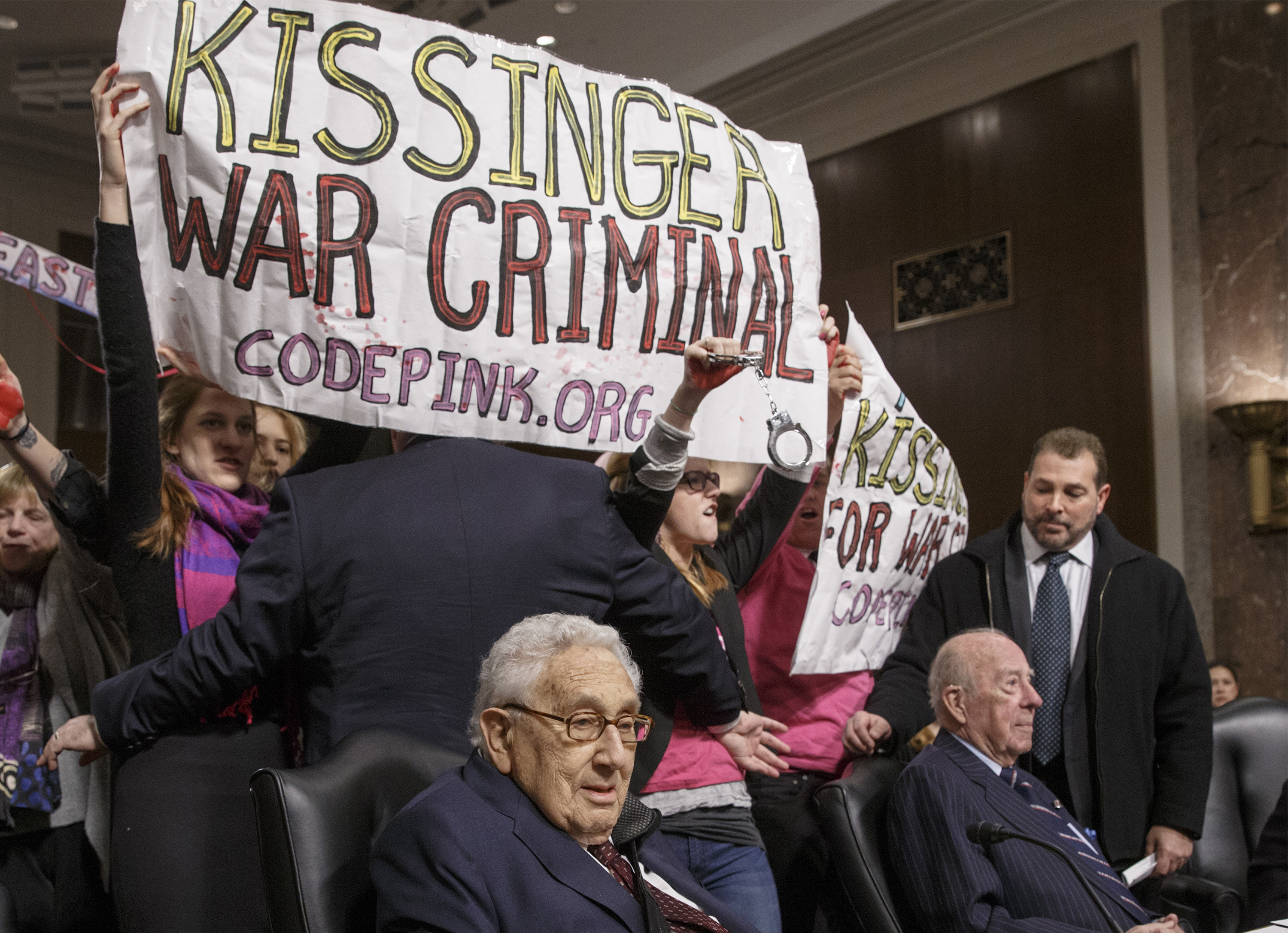 Protesters interrupt the start of a Senate Armed Services hearing as they shout at former Secretary of State Henry A. Kissinger, center, joined by former State Department head George P. Shultz, right, on Capitol Hill in Washington, Thursday, Jan. 29, 2015. The upheaval came as members of anti-war group Code Pink called the 91-year-old Kissinger a war criminal. (AP Photo/J. Scott Applewhite)