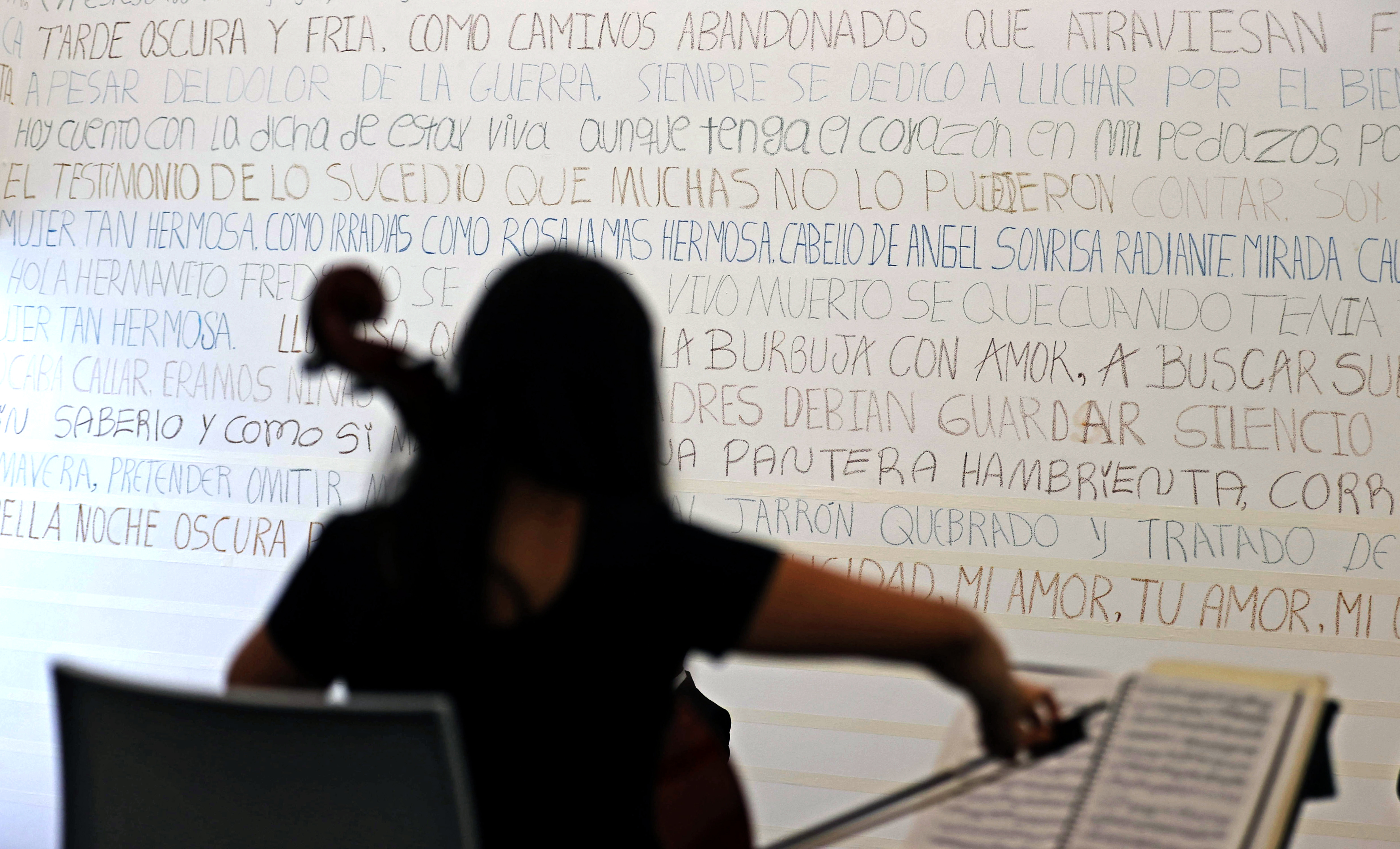 ACOMPAÑA CRÓNICA: COLOMBIA ABUSOS SEXUALES BOG200. BOGOTÁ. (COLOMBIA), 15/06/2023.- Fotografía que muestra una persona mientras toca un violín frente a un poema en el muro de Fragmentos, el 14 de junio de 2023 en Bogotá (Colombia). En "Desamadas", las 35 víctimas de violencia sexual sanan "un poco" sus tragedias con acciones de reparación simbólica, como la escritura y, más concretamente, con un poema que entre todas han escrito con la ayuda de la artista colombiana Doris Salcedo. EFE/Mauricio Dueñas Castañeda