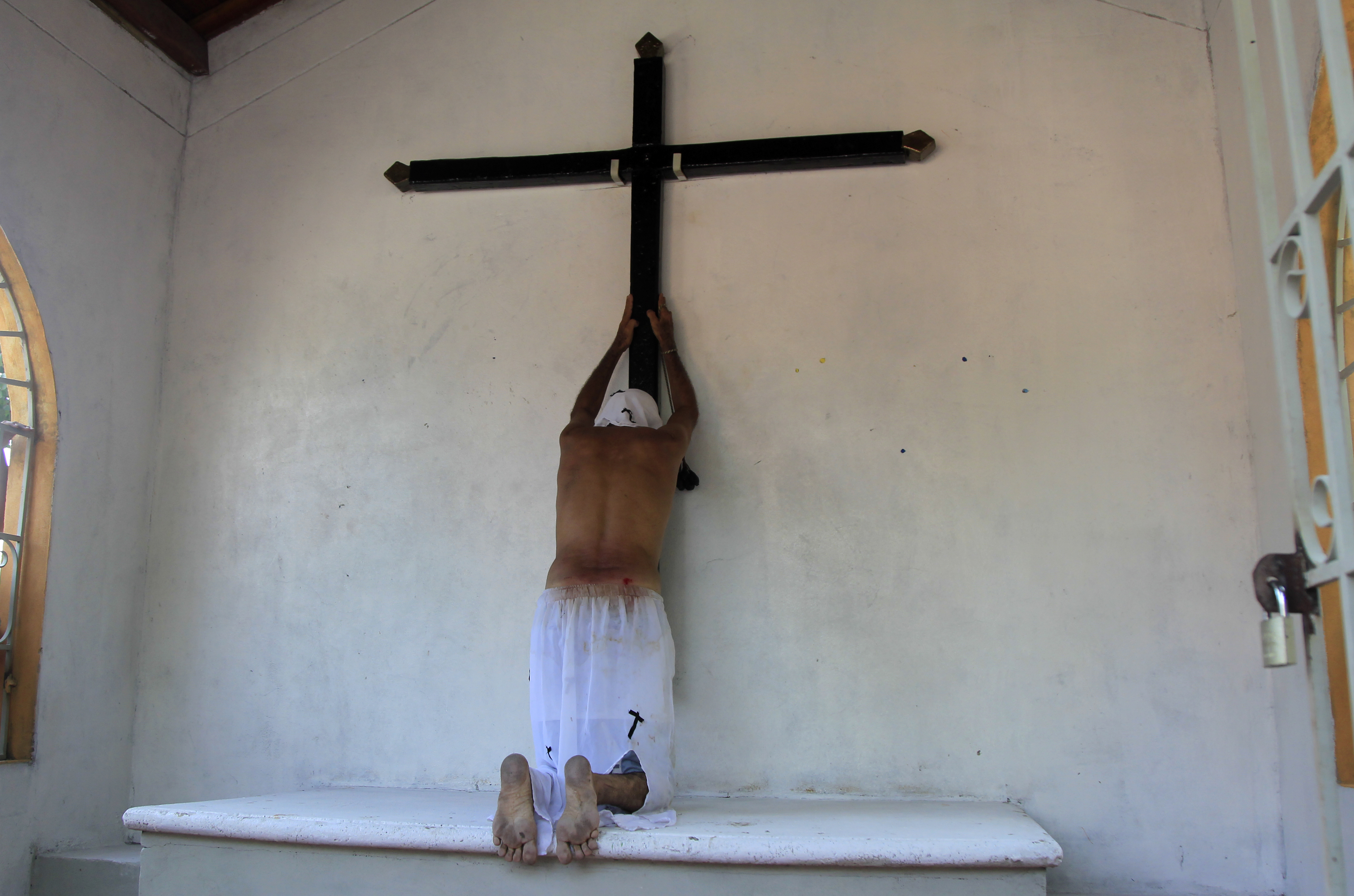 AME1608. SANTO TOMÁS (COLOMBIA), 15/04/2022.- Un flagelante ora hoy frente a una cruz en un ritual que había tenido que aplazarse durante dos años a causa de la pandemia, en Santo Tomás, Atlántico (Colombia). Por las calles de Santo Tomás, un pequeño y muy caluroso poblado colombiano aledaño a la ciudad caribeña de Barranquilla, volvieron a desfilar este viernes los penitentes, célebres por las flagelaciones que algunos de ellos se hacen en la espalda para pagar favores pedidos a Dios. EFE/ Ricardo Maldonado Rozo