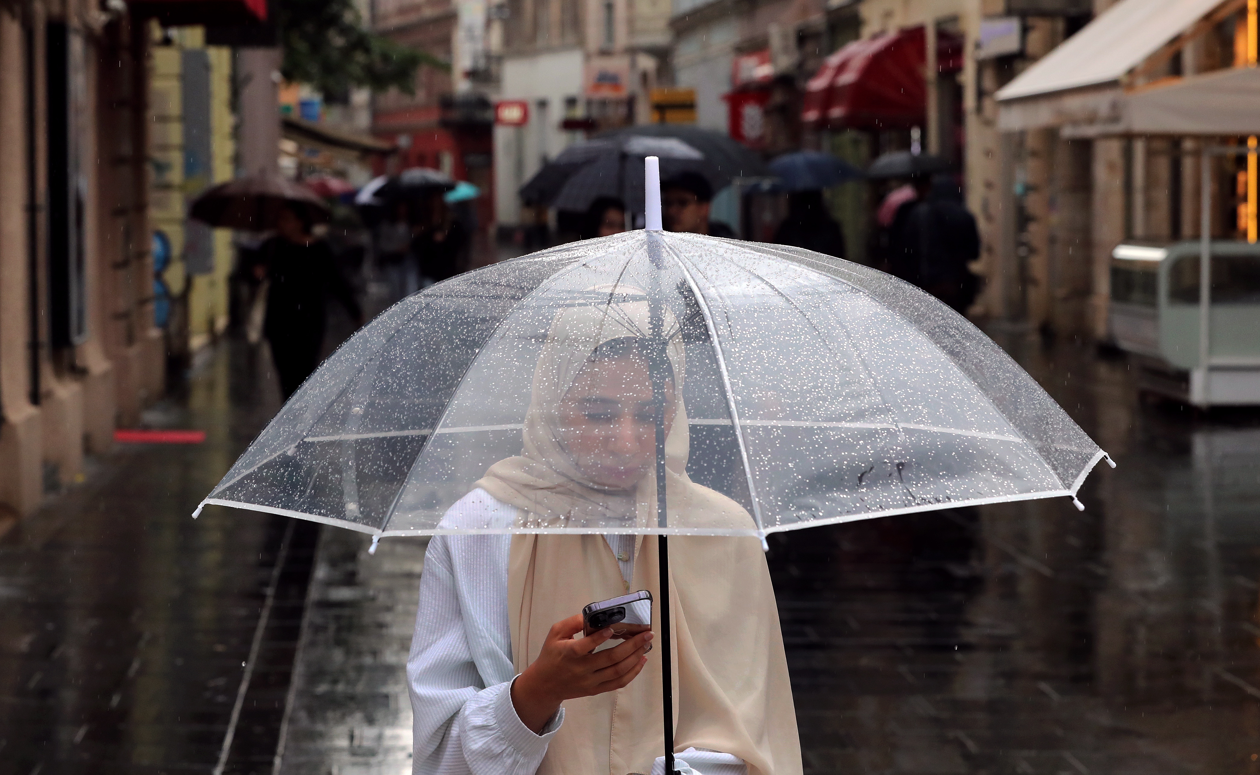 Sarajevo (Bosnia And Herzegovina), 16/06/2023.- A woman protects herself with a transparent umbrella while she uses her smartphone during a walk on a rainy day in Sarajevo, Bosnia and Herzegovina, 16 June 2023. Temperatures fell to a maximum of 14 degrees Celsius in most parts of the country stressing the observation that the Bosnian capital Sarajevo is regarded one of the coldest major cities in Southern Europe with an average hight in temperatures of just 15 degrees Celsius. (Bosnia-Herzegovina) EFE/EPA/FEHIM DEMIR