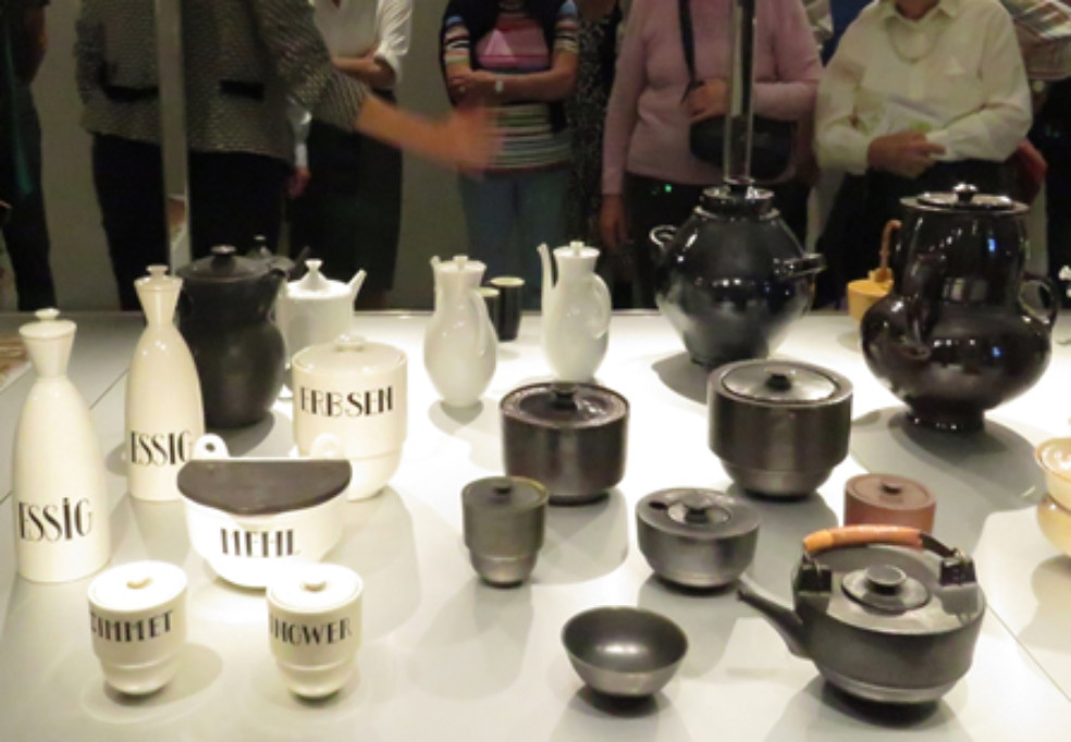 Figura 2: Visitantes observando colección cerámica de Bauhaus, Bauhaus Museum Weimar.Ingrid Quintana, 2019.La transformación del vocablo “Bauhaus” para denominar un lenguaje plástico depurado, orientado hacia el consumo doméstico, ha causado tantas divisiones entre expertos como la propia escuela. Peyorativo o elogioso, el uso intensificado de #Bauhaus en Internet durante los últimos meses ha contribuido al retorno del necesario debate sobre el impacto del diseño en múltiples dimensiones de nuestra vida cotidiana. Y es que gracias a Bauhaus y a los movimientos artísticos que le antecedieron en Austria y la URSS, la emergente producción industrial inició un diálogo tanto con las artes, gracias al cual sus patentes adquirieron una apariencia más acorde con las exigencias y gustos de los usuarios, como con las ciencias, mediante las cuales se consolidaron los principios de ergonomía, higiene y eficiencia que caracterizan sus realizaciones (figura 2).