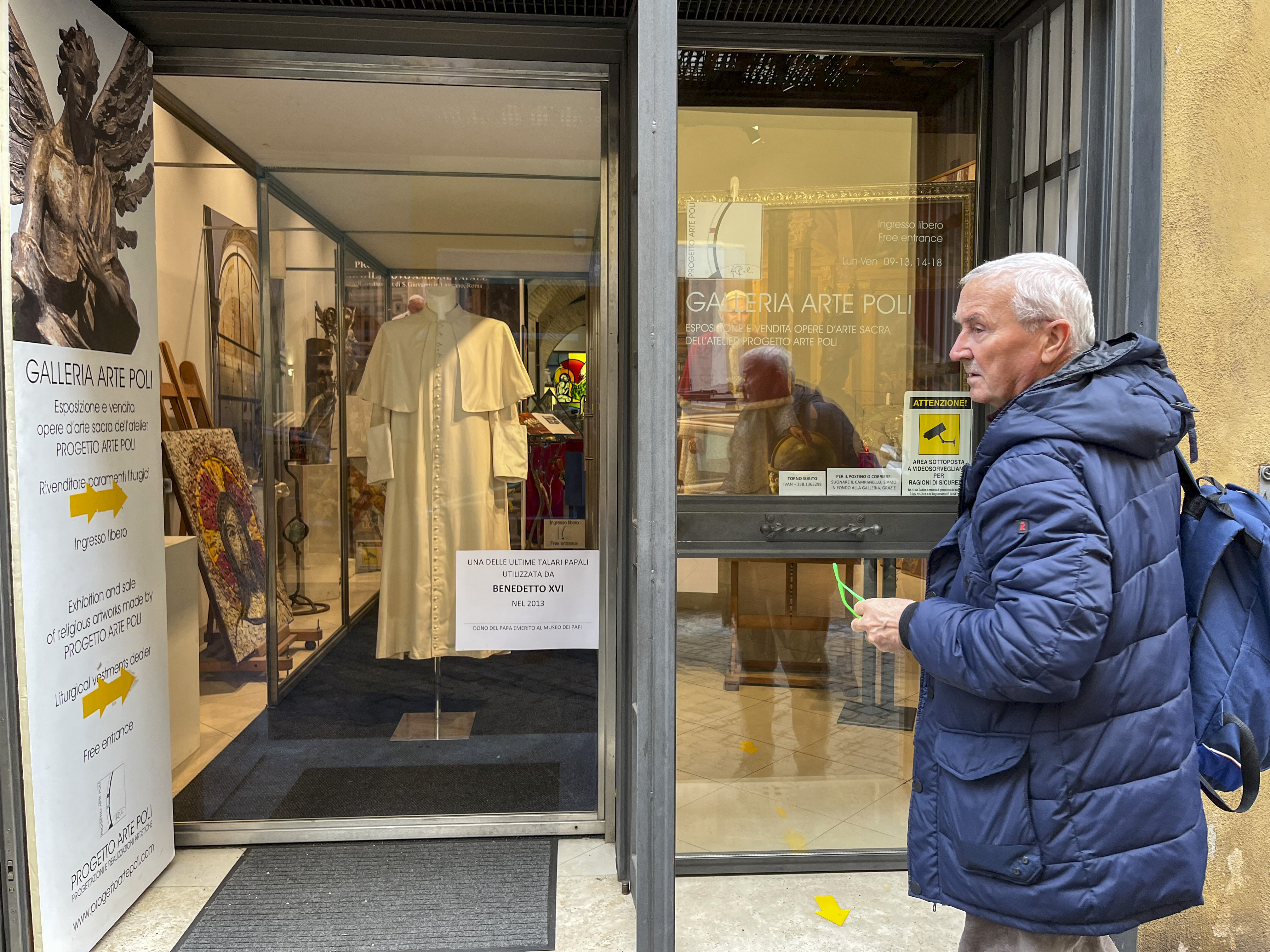 GRAF1959. CIUDAD DEL VATICANO, 03/01/2023.- Un hombre observa una sotana de Benedicto XVI expuesta en las puertas de la Galería Arte Polo del barrio romano de Borgo, junto al Vaticano. Las leyes del libre mercado afectan hasta a las cuestiones más sacras y cientos de tiendas hacen el agosto al calor del Vaticano vendiendo recuerdos y minucias con cada evento pontificio. Sin embargo, la muerte de Benedicto XVI pasa sin pena ni gloria por sus estanterías. Es el papa sin suvenires. EFE/ Gonzalo Sánchez