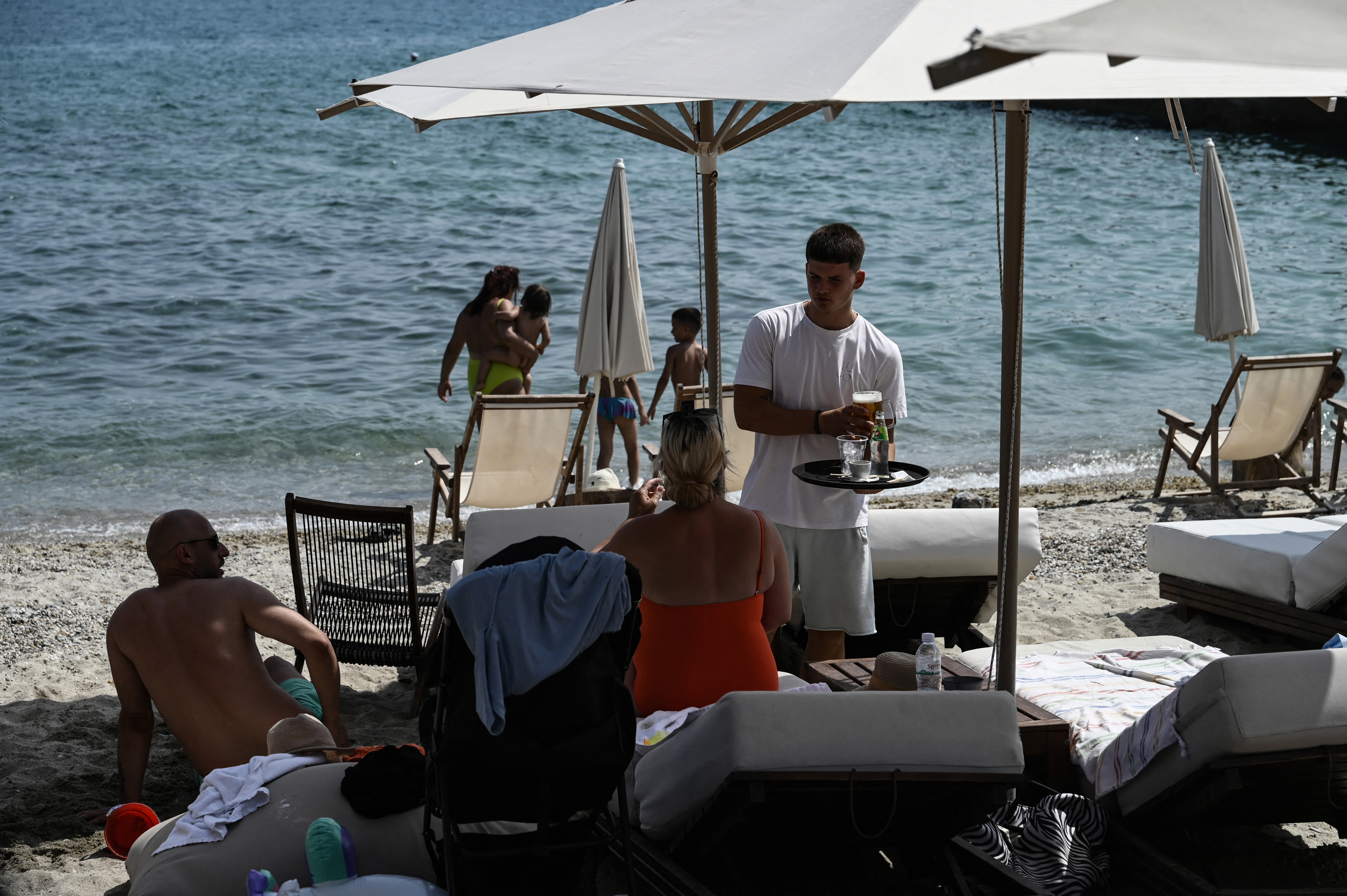 A waiter serves drinks to sunbathers sitting on their sunbeds along the beach on the Halkidiki Peninsula, northern Greece on June 13, 2025.