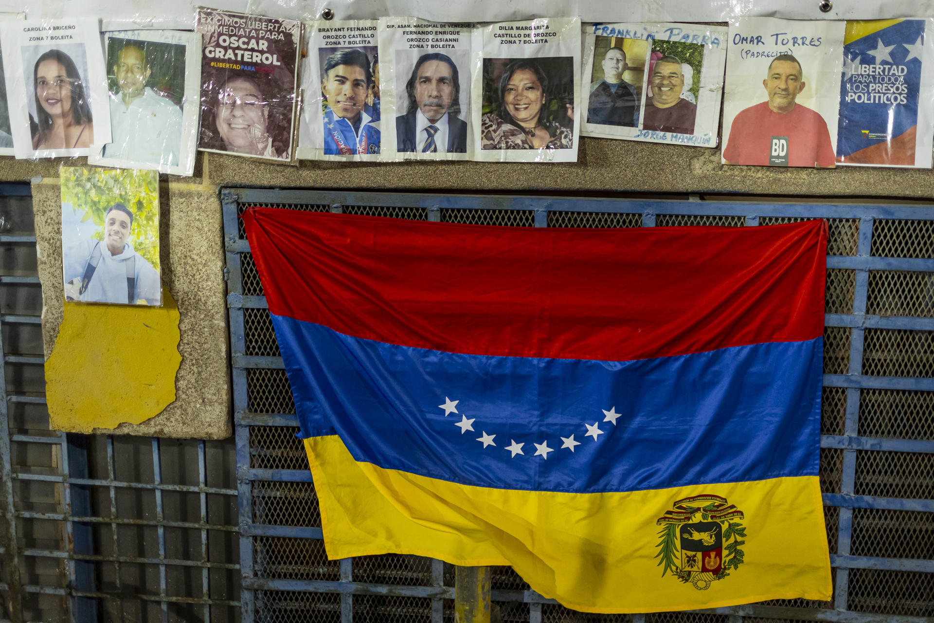 AME5750. CARACAS (VENEZUELA), 15/02/2026.- Fotografía que muestra carteles con imágenes de presos políticos y la bandera de Venezuela mientras familiares permanece en huelga de hambre a las afueras del comando de la Policía Nacional Bolivariana (PNB) conocido como Zona 7 este domingo, en Caracas (Venezuela). Dos de las diez mujeres familiares de presos políticos que desde el sábado se mantienen en huelga de hambre fuera de un comando de la PNB han sufrido problemas de salud. EFE/ Miguel Gutiérrez