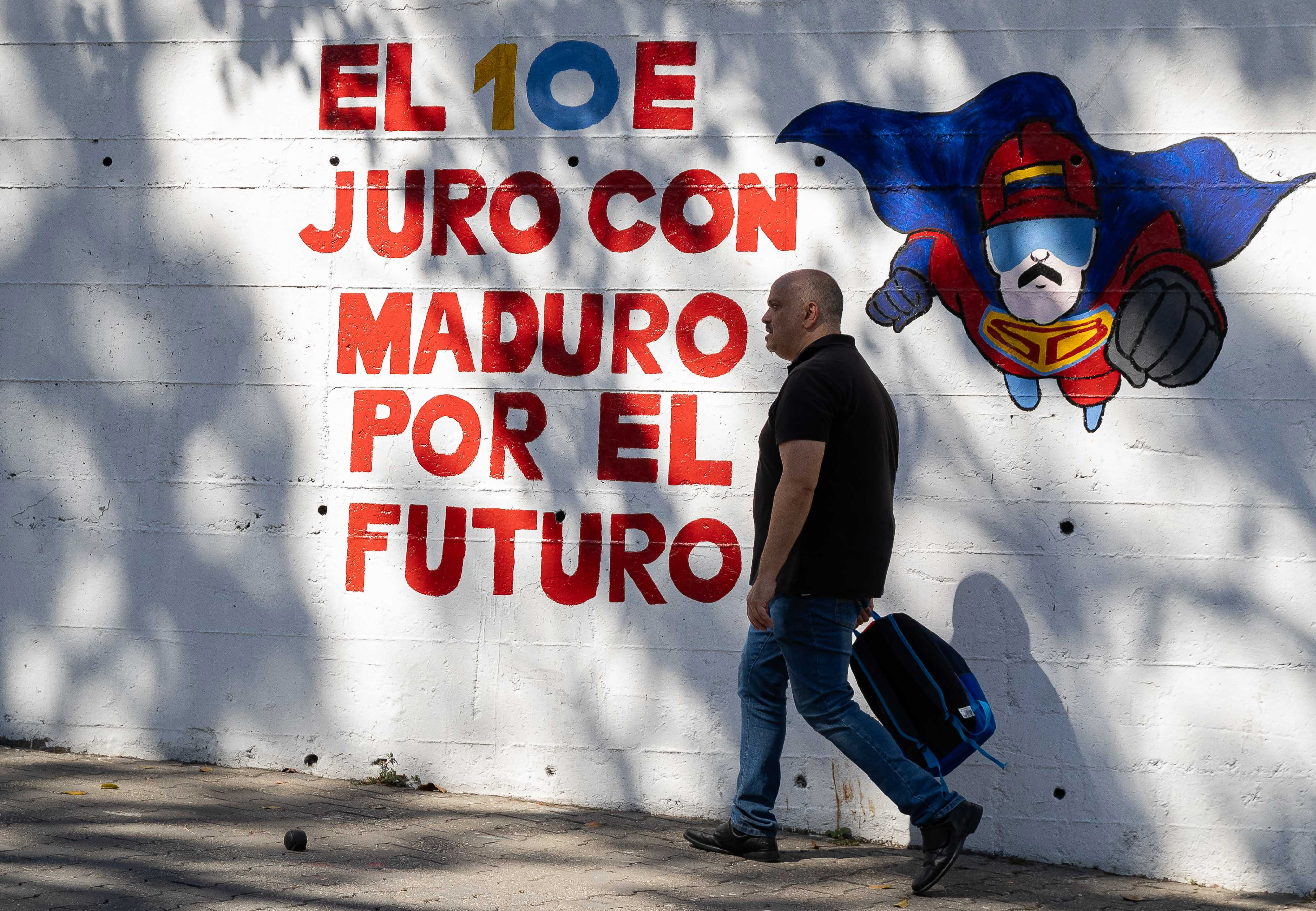 AME5368. CARACAS (VENEZUELA), 15/12/2024.- Un hombre camina frente a un mural con el mensaje "El 10E juro con Maduro por el futuro" este viernes, en Caracas (Venezuela). La Constitución de Venezuela llega este domingo a sus 25 años con un cuestionado cumplimiento de sus preceptos y un país alejado del descrito en la carta magna -aprobada en referendo popular el 15 de diciembre de 1999-, de lo que se acusan mutuamente el chavismo y la oposición. EFE/ Ronald Peña R.