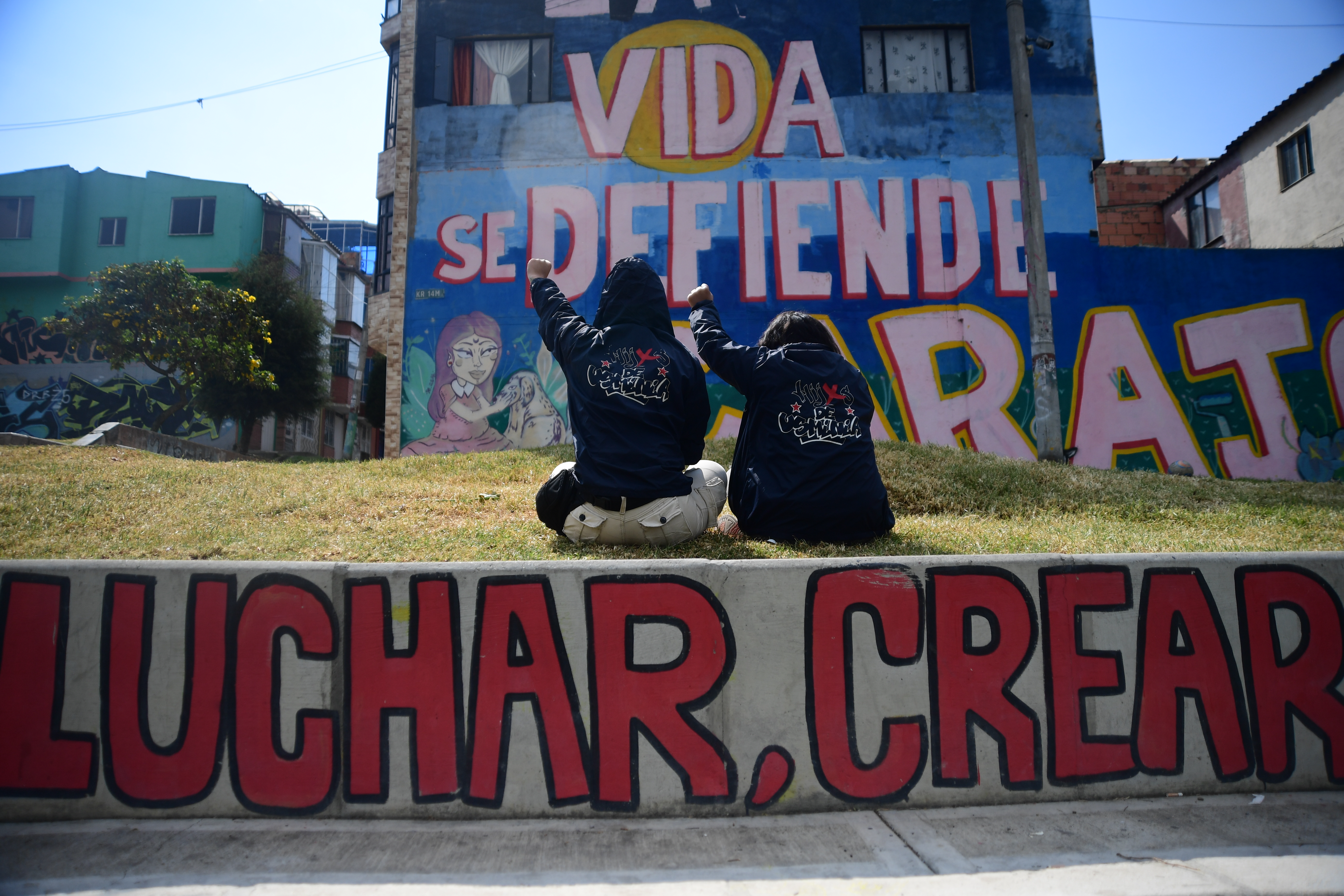Dos mujeres de espaldas frente a un mural que dice "Vida se defiende"