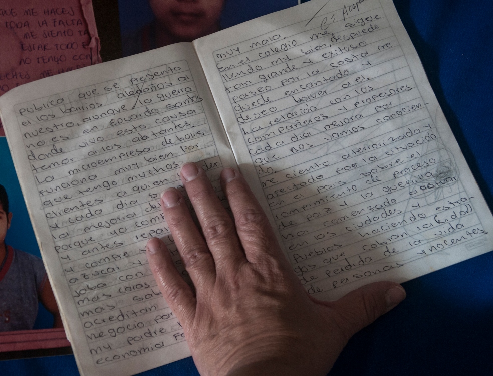 Un cuaderno de un niño con anotaciones y la mano de un adulto sobre él.