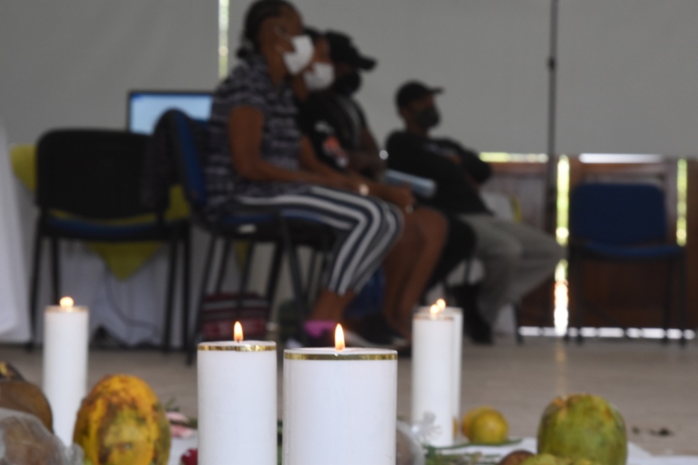 primer plano un grupo de velas encendidas y, en segundo plano, un grupo de personas  sentadas.
