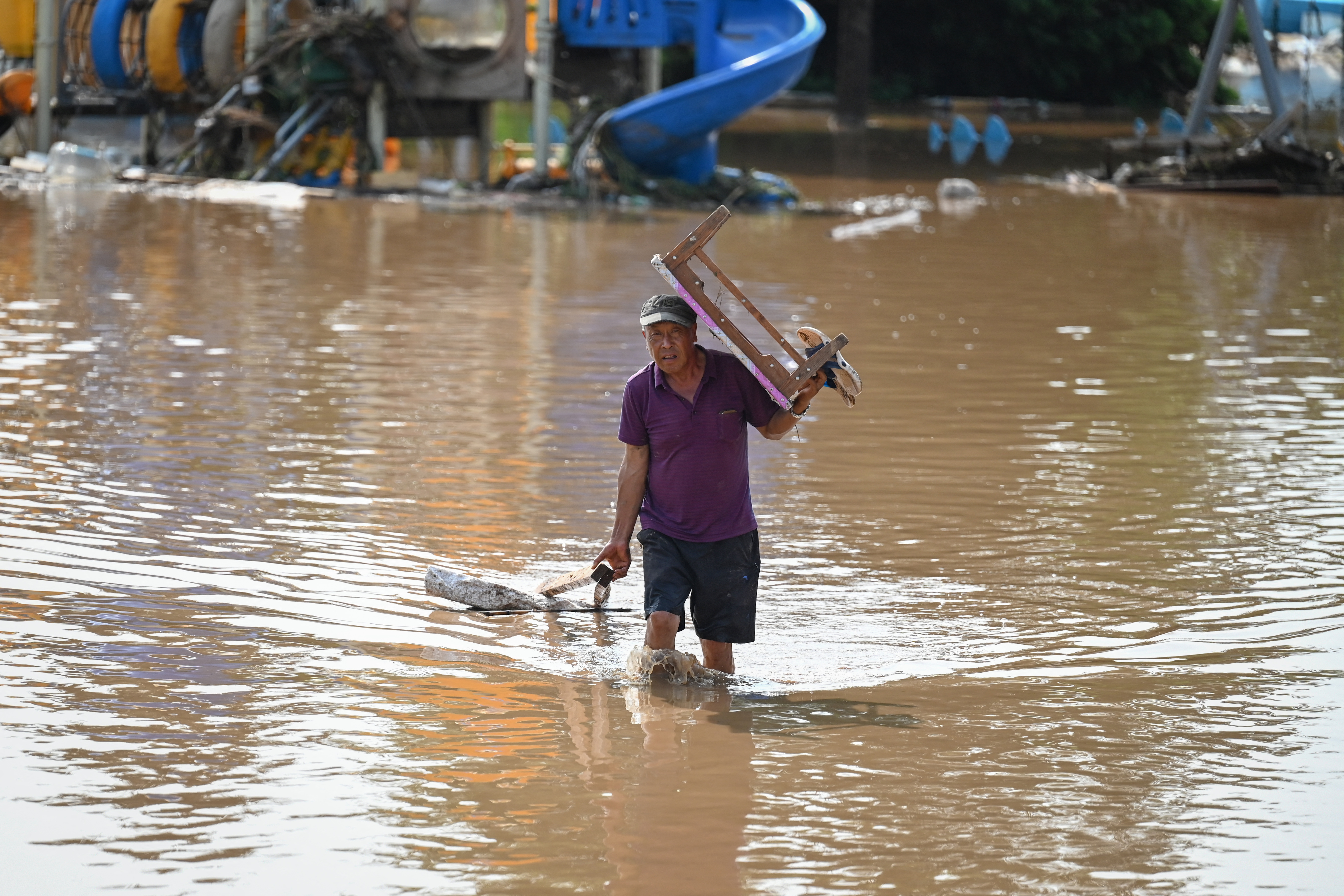 A resident carrying a table walks through a flooded area after heavy rains at Taishitun village in Miyun district, on the outskirts of Beijing on July 28, 2025.