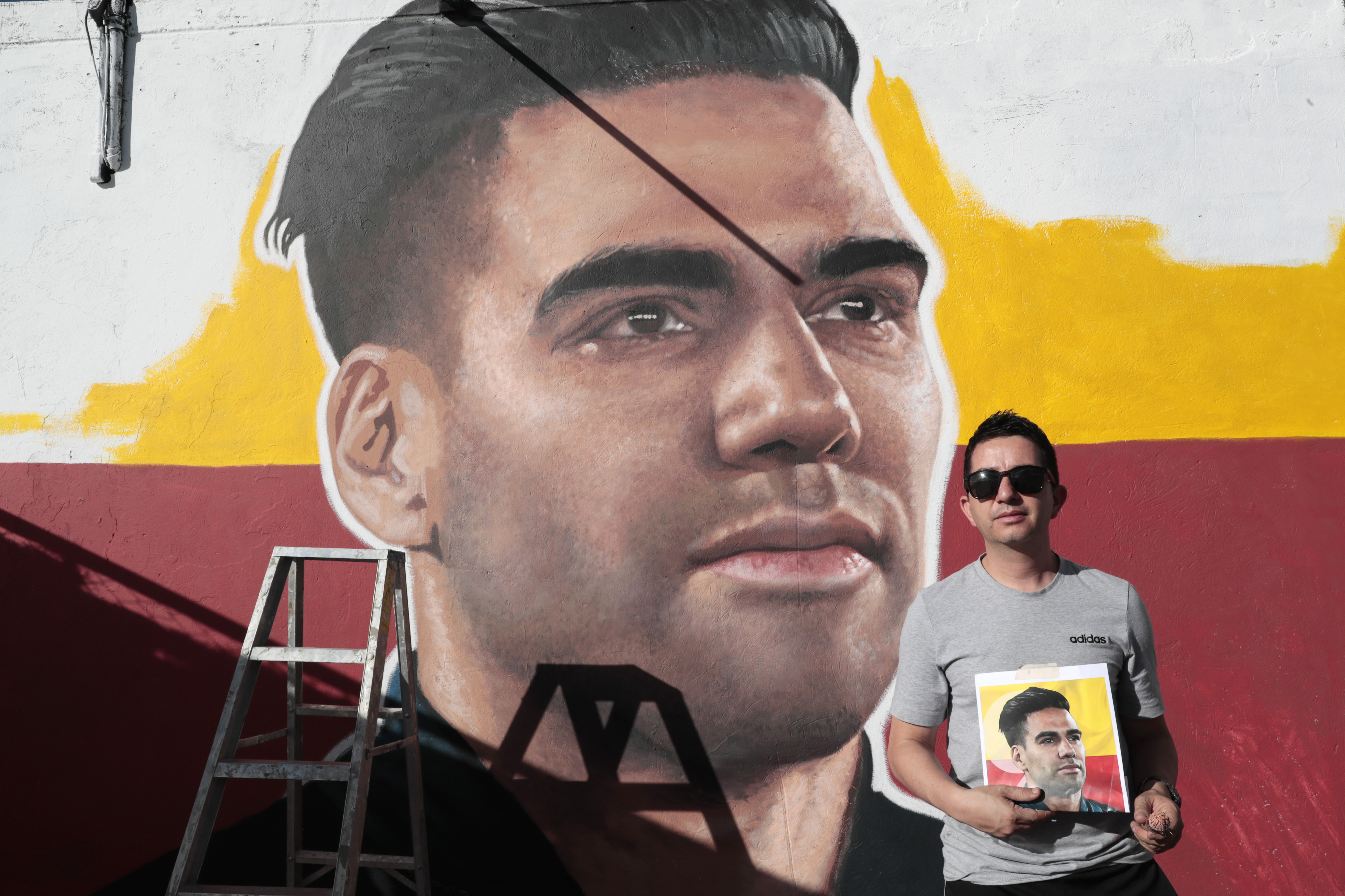 AME8840. BOGOTÁ (COLOMBIA), 02/07/2024.- El artista Emerson Cáceres, conocido como Cacerolo, posa junto a un mural con el rostro del futbolista colombiano Radamel Falcao García en una de las paredes del exterior del estadio Nemesio Camacho ' El Campín', este martes en Bogotá (Colombia). Un mural de Falcao García es pintado en una de las paredes del estadio El Campín de Bogotá con motivo de fichaje del experimentado futbolista colombiano por Millonarios. 'Cacerolo' asegura a EFE: "Para los hinchas del Millonarios es un orgullo tener a Falcao en el equipo, uno de los mejores 9 del fútbol mundial". EFE/ Carlos Ortega