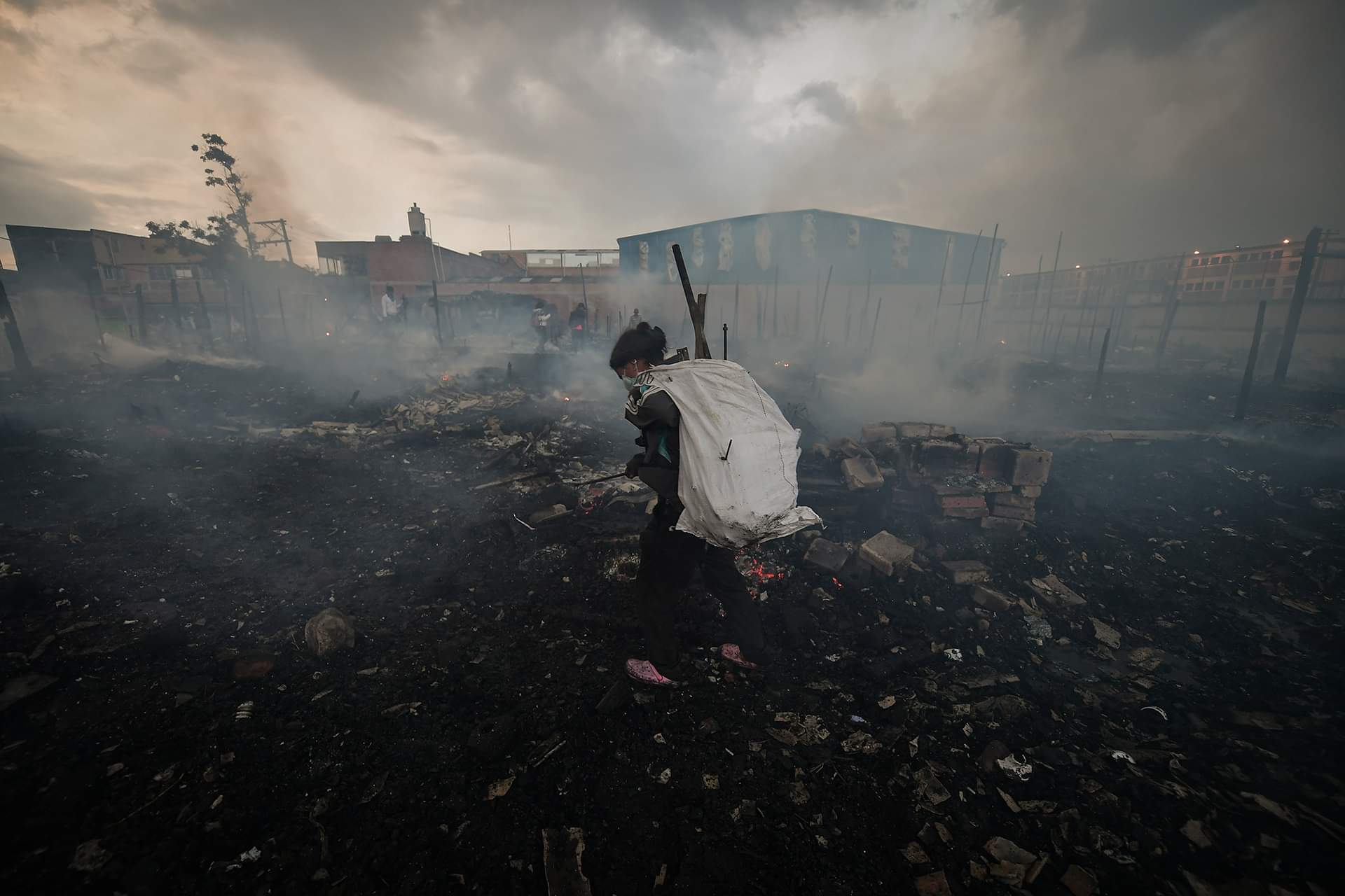 Una mujer carga un costal blanco entre los escombros del incendio.