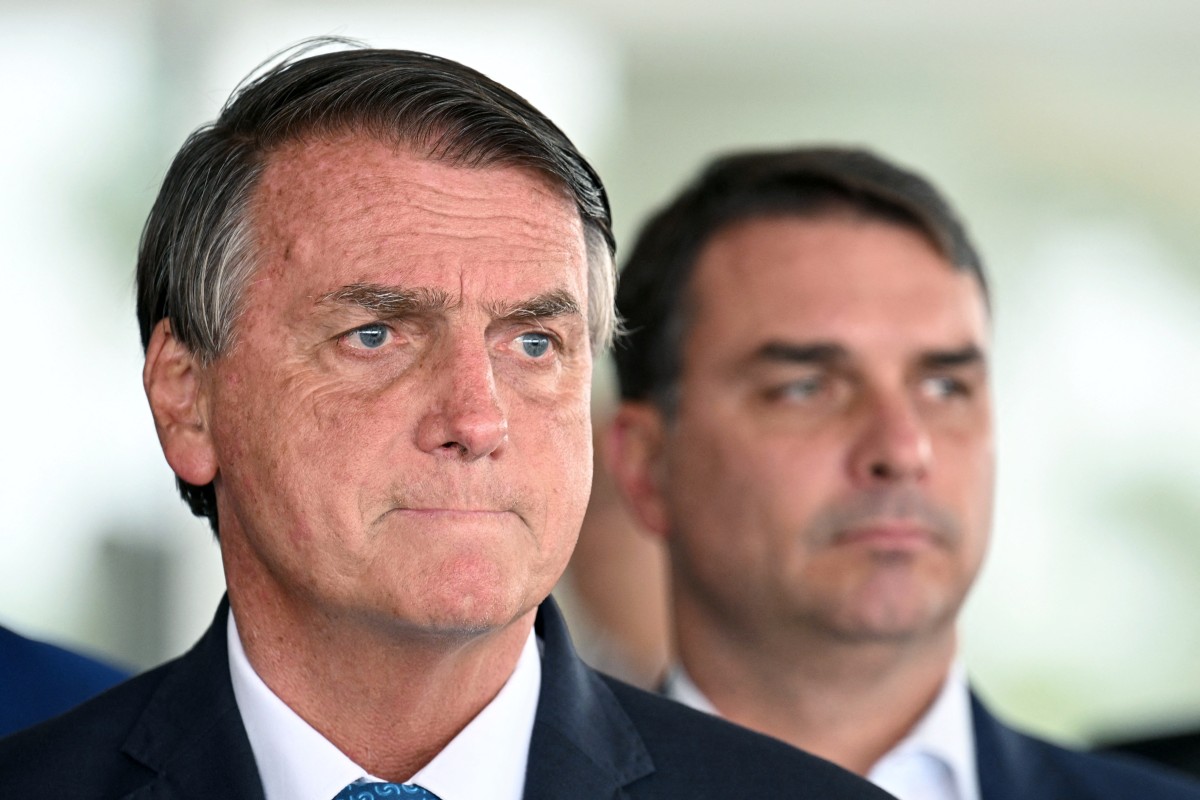 (FILES) Brazilian President and re-election candidate Jair Bolsonaro (L) listens to questions next to his son Flavio during a press conference at Planalto Palace in Brasilia, on October 4, 2022.