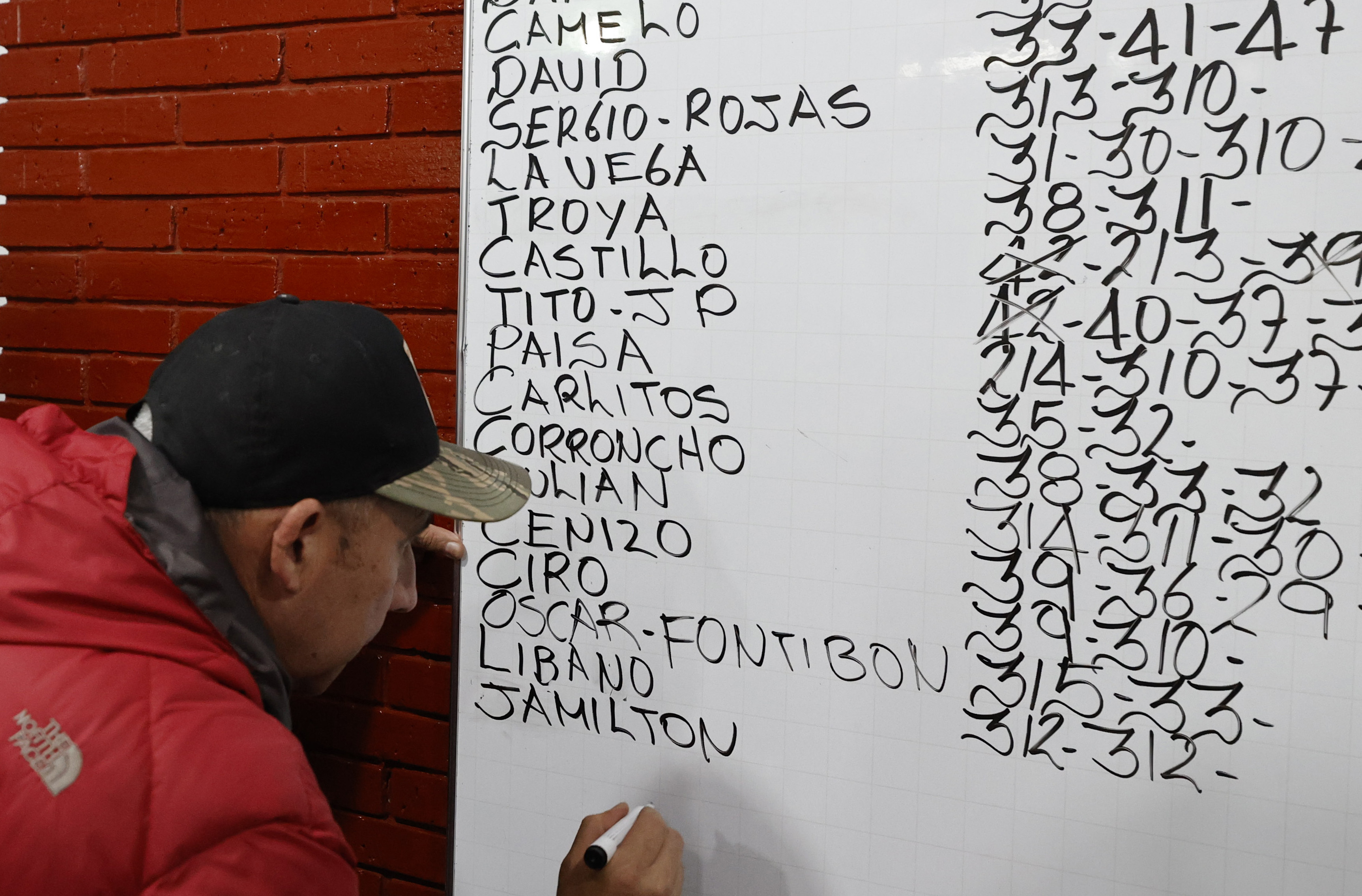 ACOMPAÑA CRÓNICA: COLOMBIA ANIMALES. BOG300. BOGOTÁ (COLOMBIA), 02/11/2022.- Un hombre escribe el peso de los gallos previo a una pelea, el 21 de octubre de 2022, en Bogotá (Colombia). En la pizarra de la entrada, con una caligrafía casi perfecta, los dueños de la gallera van anotando los rivales de la noche: los gallos no tienen nombre, no es relevante, pero sí lo es el peso y el tamaño para enfrentarlos en "condiciones justas" en un espectáculo que ha quedado atrapado en el tiempo en Colombia.EFE/ Mauricio Dueñas Castañeda