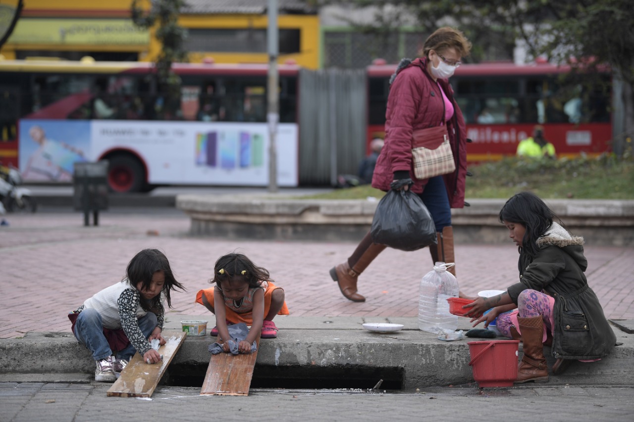 Niños indígenas lavan tapabocas en un costado de una acera en la calle.