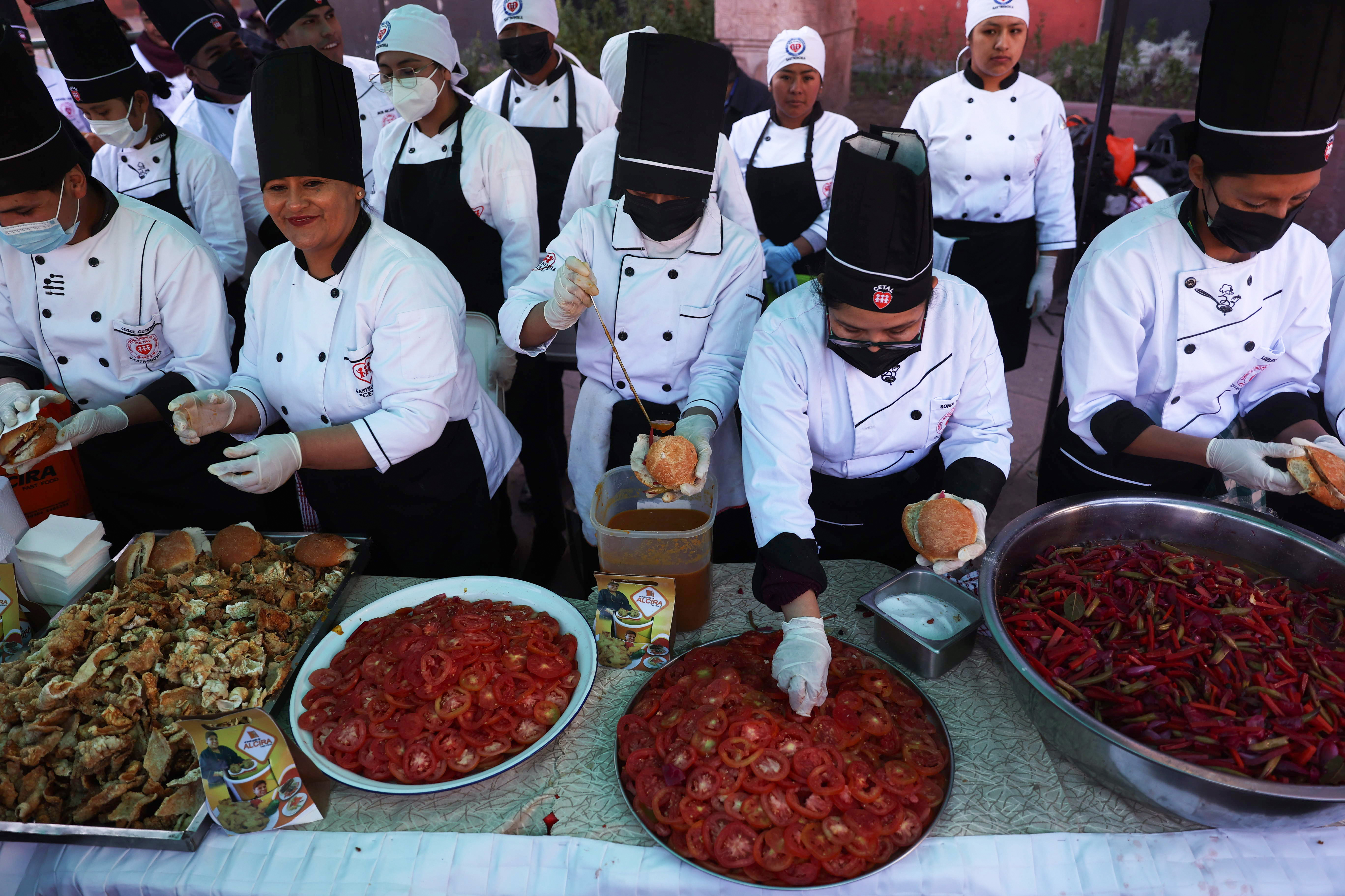 AME8795. LA PAZ (BOLIVIA), 02/07/2024.- Cocineros preparan salsas durante la presentación del Sandwich de chola más grande del mundo, este martes en La Paz (Bolivia). Un centenar de cocineros de Bolivia prepararon durante dos días un sándwich de más de dos metros de diámetro, y lo presentaron este martes frente a decenas de bolivianos, en un evento para reivindicar la gastronomía de la ciudad de La Paz y sus ingredientes y la comida tradicional. EFE/ Luis Gandarillas