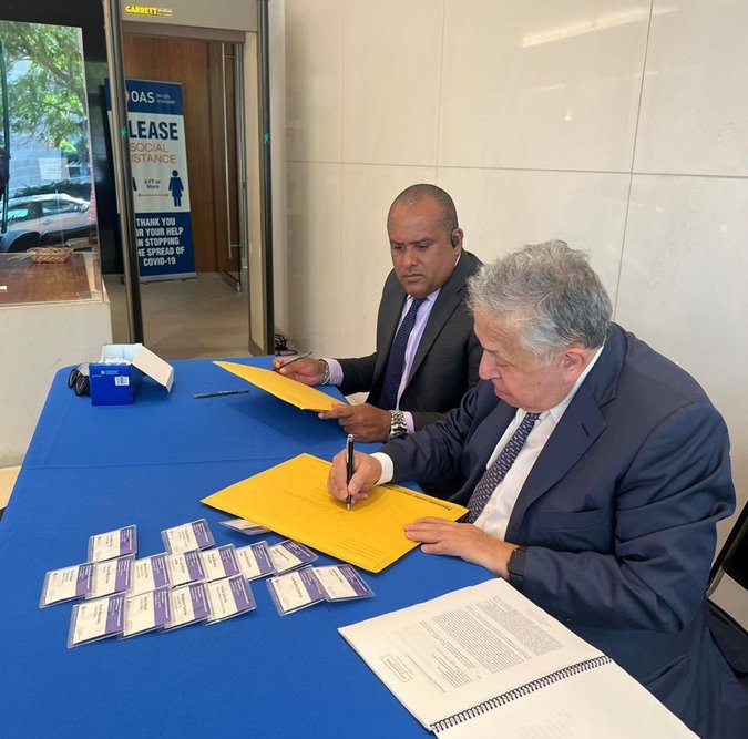 Sobre una mesa de base color azul, el gobernador de San Andrés y su abogado suscriben el documento para solicitar medida de protección ante la comisión interamericana de derechos humanos.