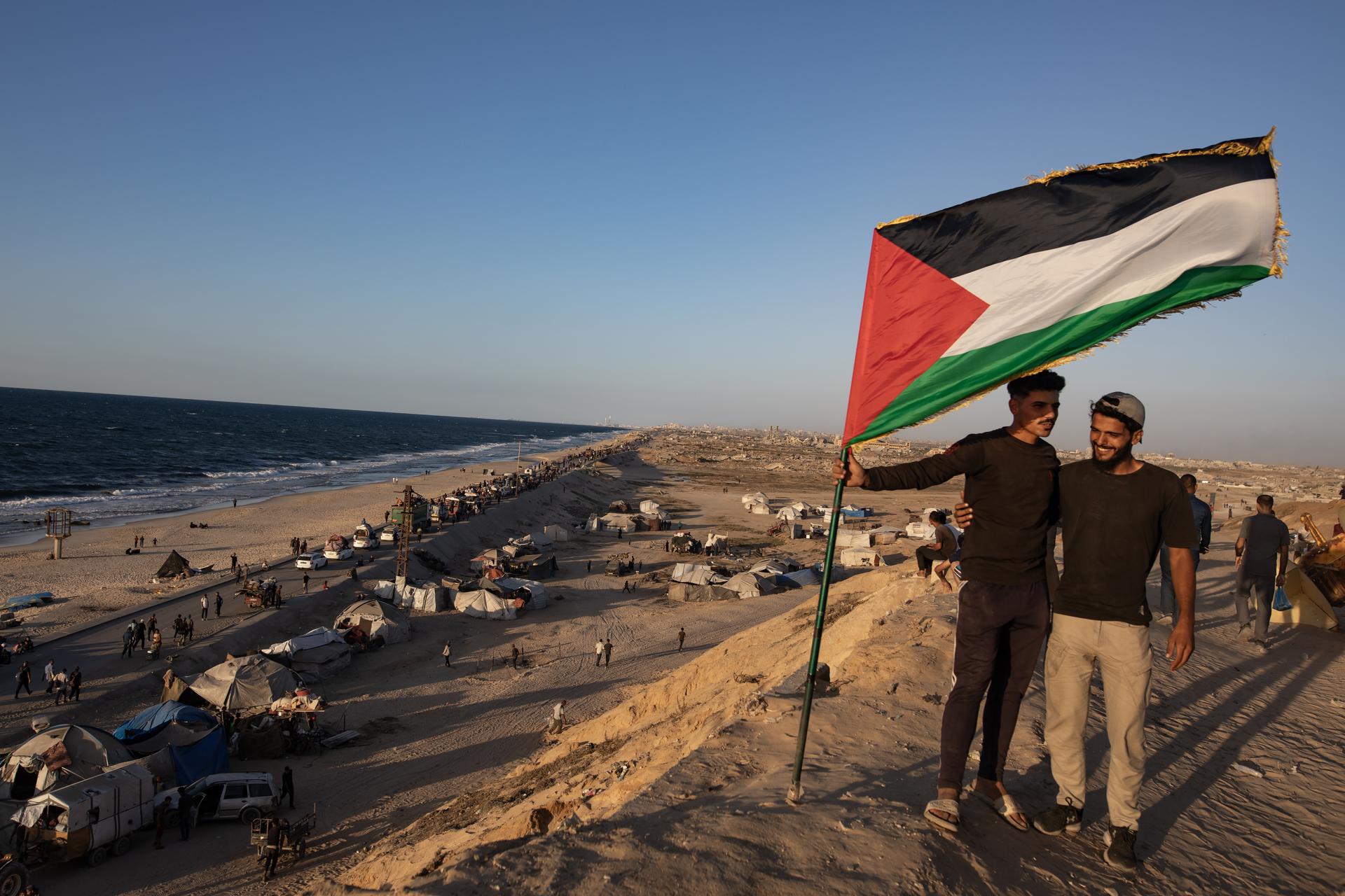 GAZA (---), 10/10/2025.- Two men pose with the Palestine flag as displaced Palestinians walk carrying their belongings along the Al-Rashid coastal road near Wadi Gaza in the central Gaza Strip, heading toward Gaza City, 10 October, 2025. Israeli Prime Minister Benjamin Netanyahu's office announced on 09 October that the Israeli government had approved the Gaza ceasefire and hostage release plan. EFE/EPA/HAITHAM IMAD

