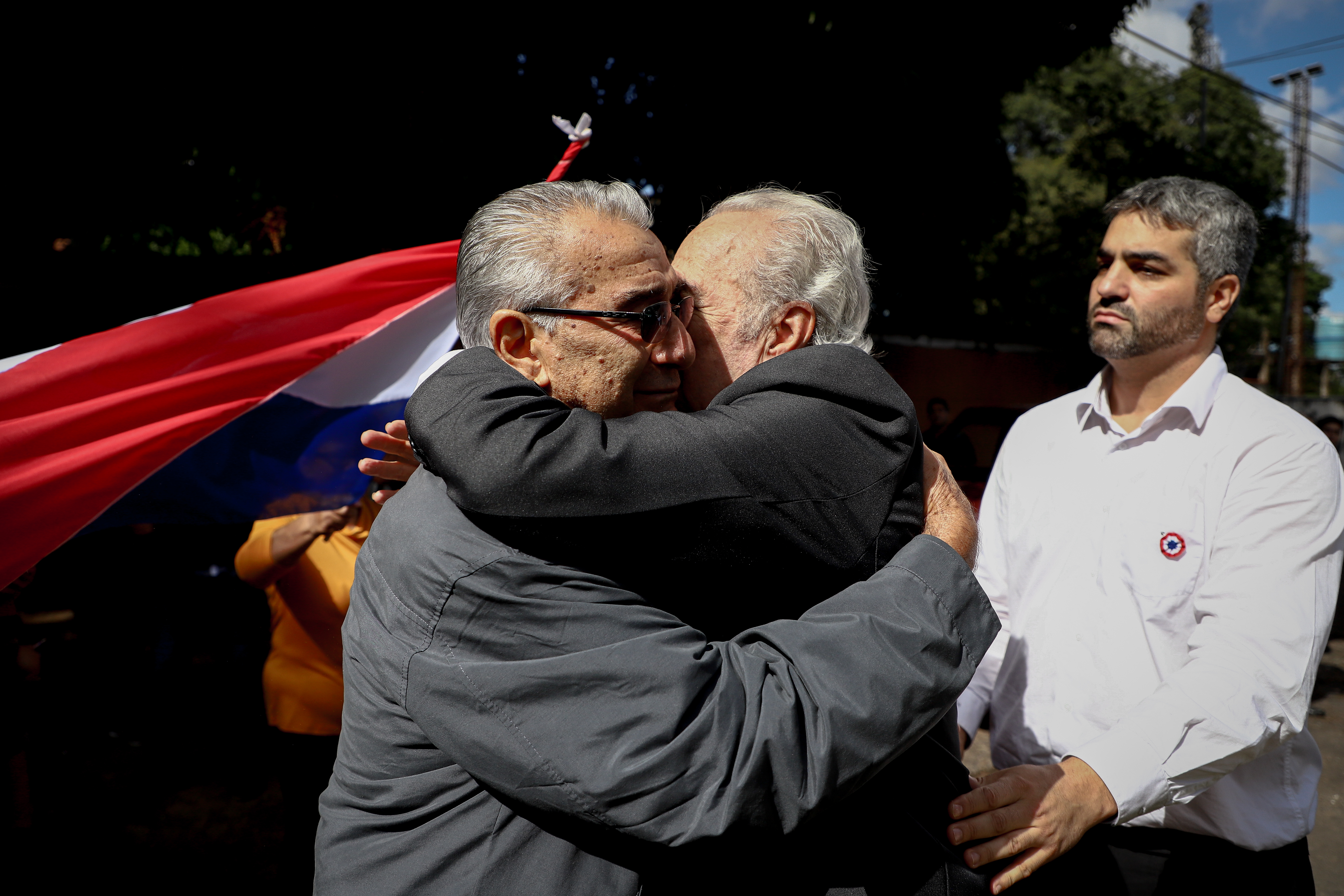 AME9535. ASUNCIÓN (PARAGUAY), 15/05/2022.- Francisco Pecci (c), padre del asesinado fiscal Marcelo Pecci, abraza hoy a un dirigente del Club Guaraní en Asunción (Paraguay). Marcelo Pecci, el fiscal asesinado en Colombia y a quien este domingo despiden los paraguayos, se erigió públicamente en implacable contra el delito, pero para sus allegados era el hombre de buen humor, apasionado por el fútbol y la aviación. Asimismo, dirigentes, futbolistas y fanáticos del Club Guarani le rinden un homenaje al fiscal Pecci en la sede del club. EFE/ Nathalia Aguilar