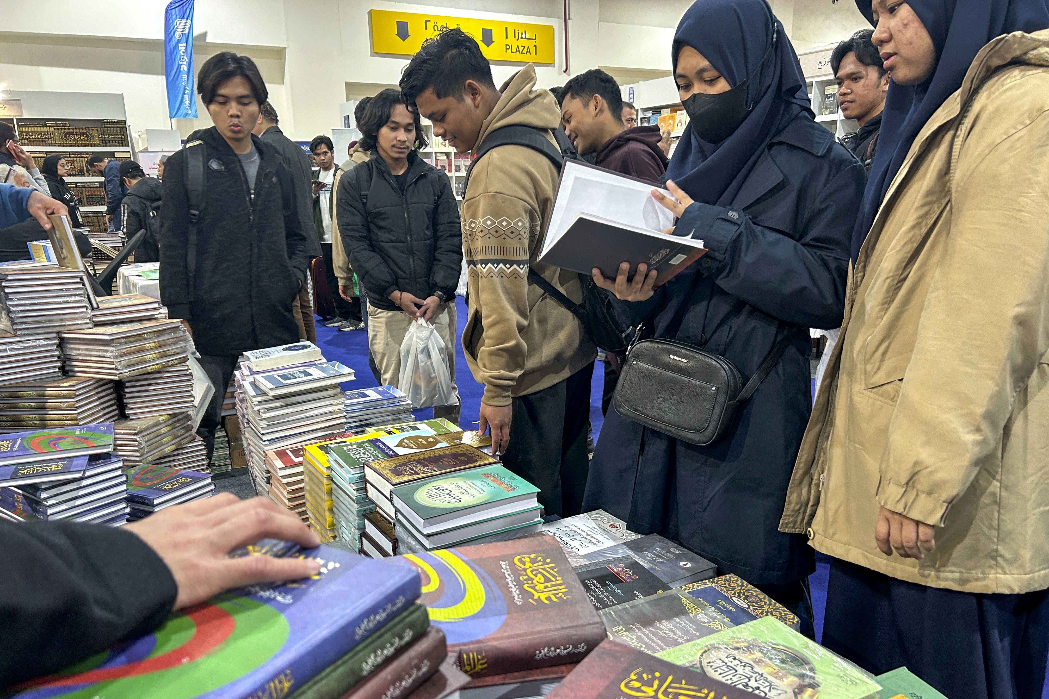 EL CAIRO, 06/02/2024.- Un grupo de estudiantes malasios con indumentaria islámica hojean las páginas de un Corán de edición coleccionista en uno de los puestos de la Feria del Libro del Cairo, la más importante del Oriente Medio y una de las más grandes del mundo. Son alumnos de la universidad Al Azhar, situada en el Cairo y una de las más prestigiosas del mundo islámico en cuanto a estudios religiosos, y han venido a la feria, la más importante de Oriente Medio y una de las mayores del mundo, según explica uno de ellos en un árabe no muy fluido, a proveerse de material religioso. La Feria del Libro de El Cairo atrae a más de 2 millones de visitantes al año, y, al menos este año, destina uno de sus cinco pabellones enteramente a casas de publicación religiosas, una temática que también ocupa a decenas de otros expositores repartidos a lo largo y ancho de la feria.- EFE/ Helena Pelicano