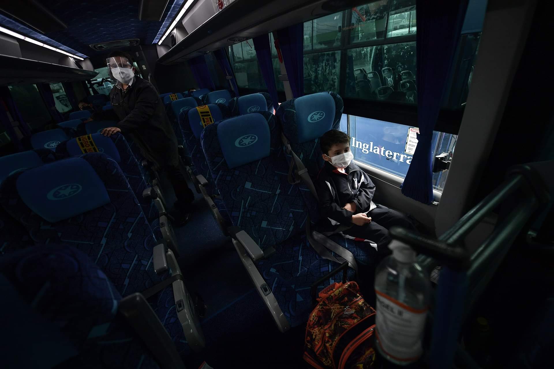 Un niño sentado en una silla y la monitora de la ruta en el pasillo.