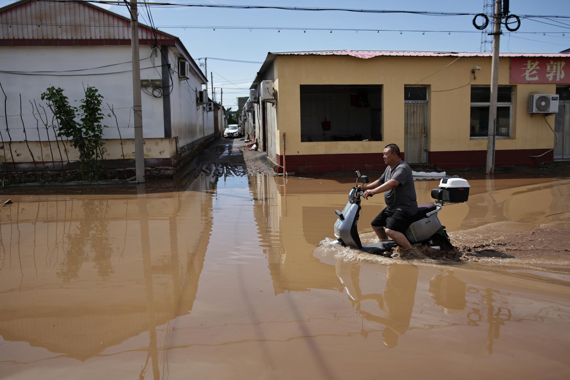 BEIJING (China), 29/07/2025.- A man tries to drive an electric moped along a flooded street at Taishitun, in the district of Miyun, Beijing, China, 29 July 2025. The floods brought on by the rains in past days in Beijing resulted in the deaths of thirty people and the relocation of over 80,000 others. (Inundaciones) EFE/EPA/ANDRES MARTINEZ CASARES