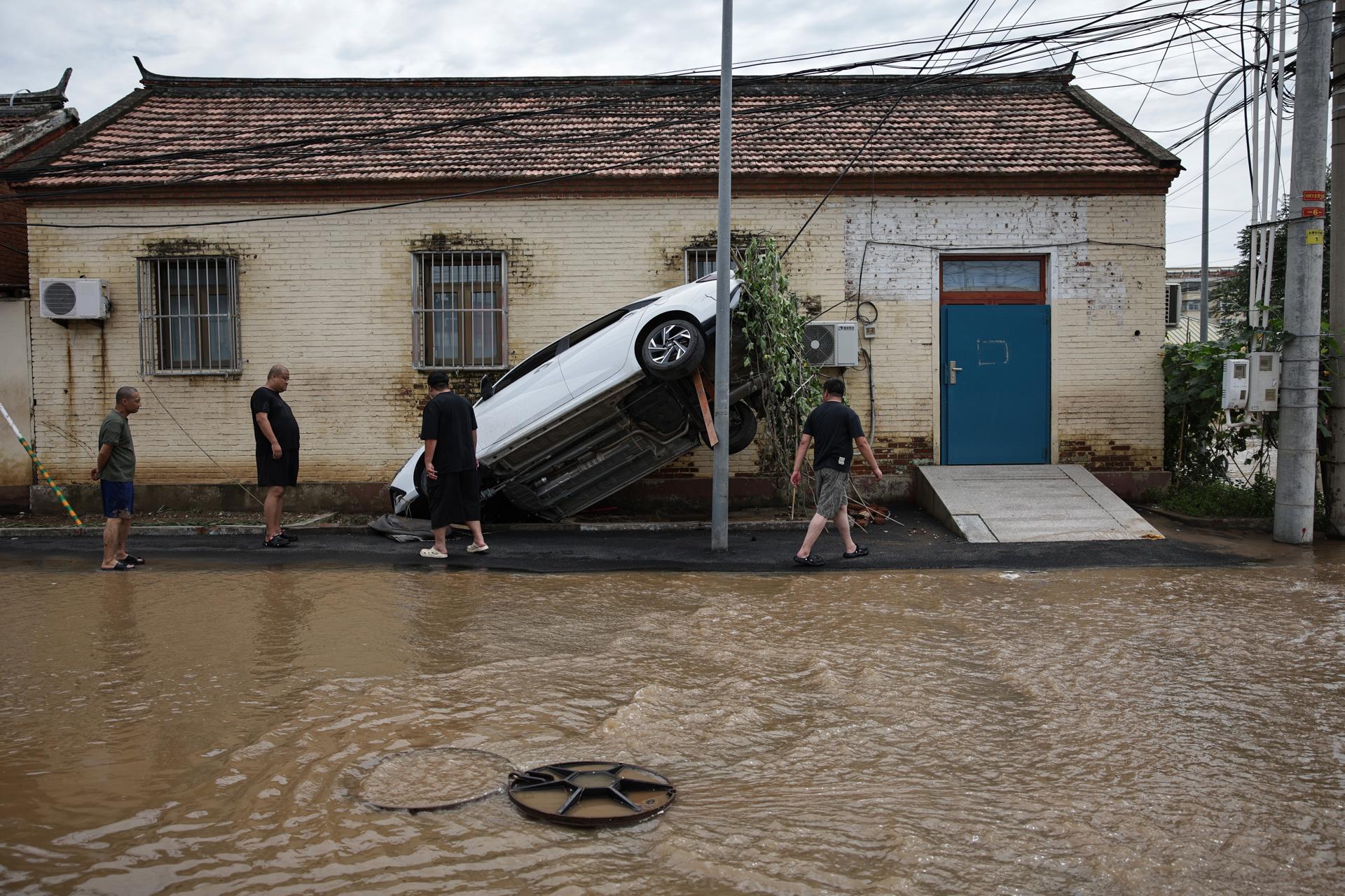 BEIJING (China), 29/07/2025.- Four men look at a car whased away by flooding in Taishitun, in the district of Miyun, Beijing, China, 29 July 2025. The floods brought on by the rains in past days in Beijing resulted in the deaths of thirty people and the relocation of over 80,000 others. (Inundaciones) EFE/EPA/ANDRES MARTINEZ CASARES
