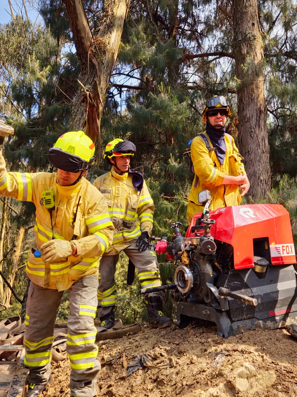 Bomberos prueban la presión de una motobomba a pocos metros del punto más crítico del incendio.