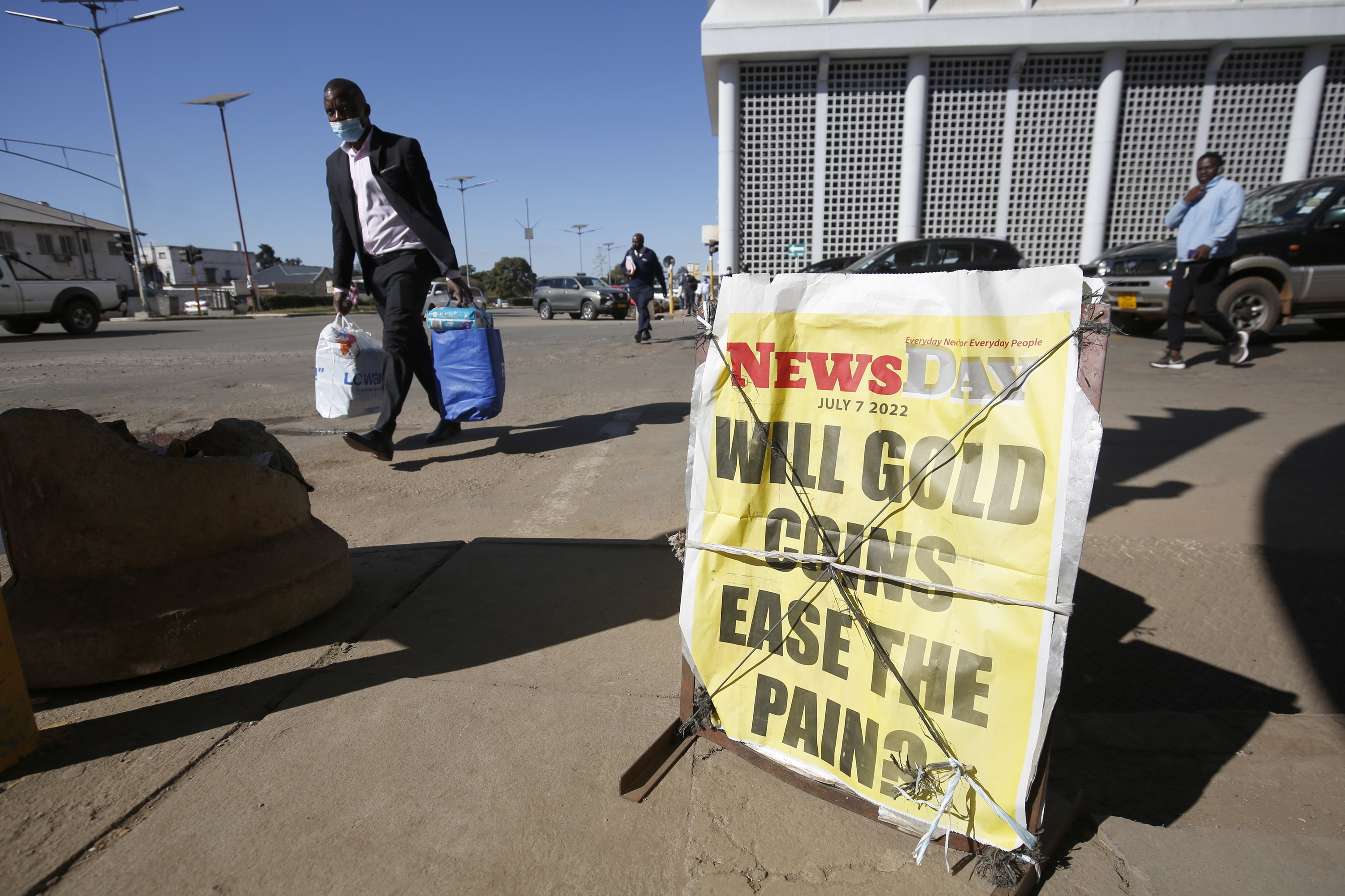 Harare (Zimbabwe), 07/07/2022.- Members of the public walk past a newspaper poster with a headline on the introduction of gold coins in Harare, Zimbabwe, 07 July 2022. The Reserve Bank of Zimbabwe governor John Mangudya announced on 27 June 2022 the move as the economic crisis continue to wreck havoc, that Zimbabwe will start selling gold coins in July 2022 in a bid to tackle runaway inflation which has hamstrung the local currency. The gold coin is named 'Mosi-oa-Tunya', after Victoria Falls, and can be converted into cash. (Zimbabue) EFE/EPA/AARON UFUMELI