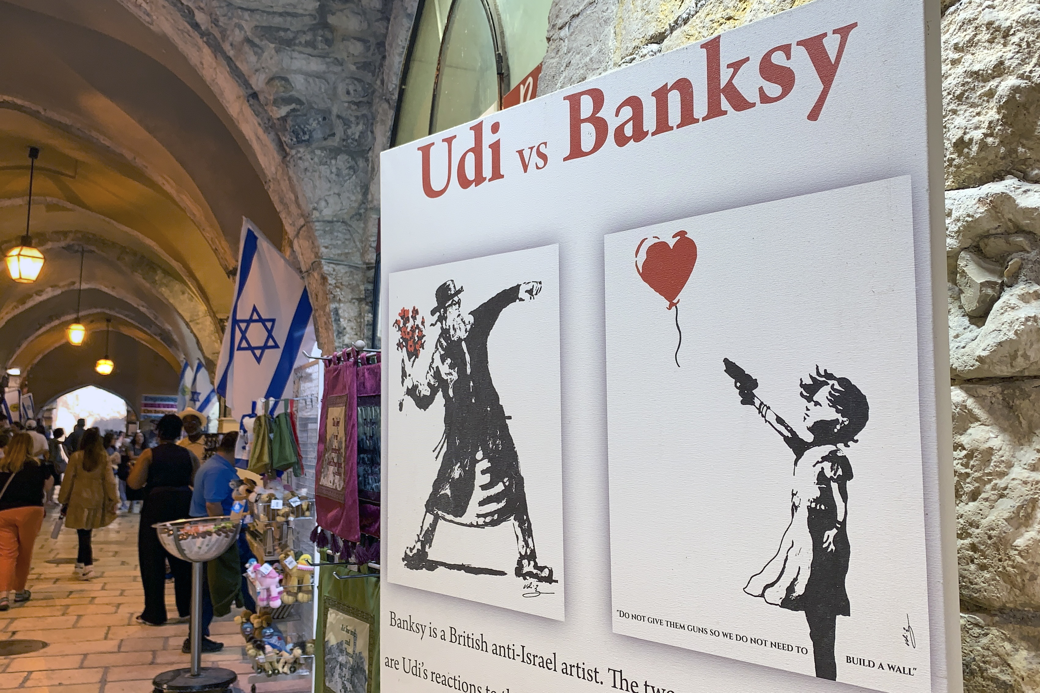 JERUSALÉN, 01/09/2023.- Un cartel muestra las obras "No les den armas para que no tengamos que construir un muro, y se encontrarán con flores" del pintor israelí Udi Merioz, en contraposición a la obra del artista Banksy, "Niña con globo", en Jerusalén este viernes. Desde su taller en Jerusalén, el pintor judío Udi Merioz alza su pincel y libra una batalla iconográfica contra el artista callejero Bansky y sus famosísimos grafitis de protesta contra la ocupación israelí. EFE/ Yemeli Ortega