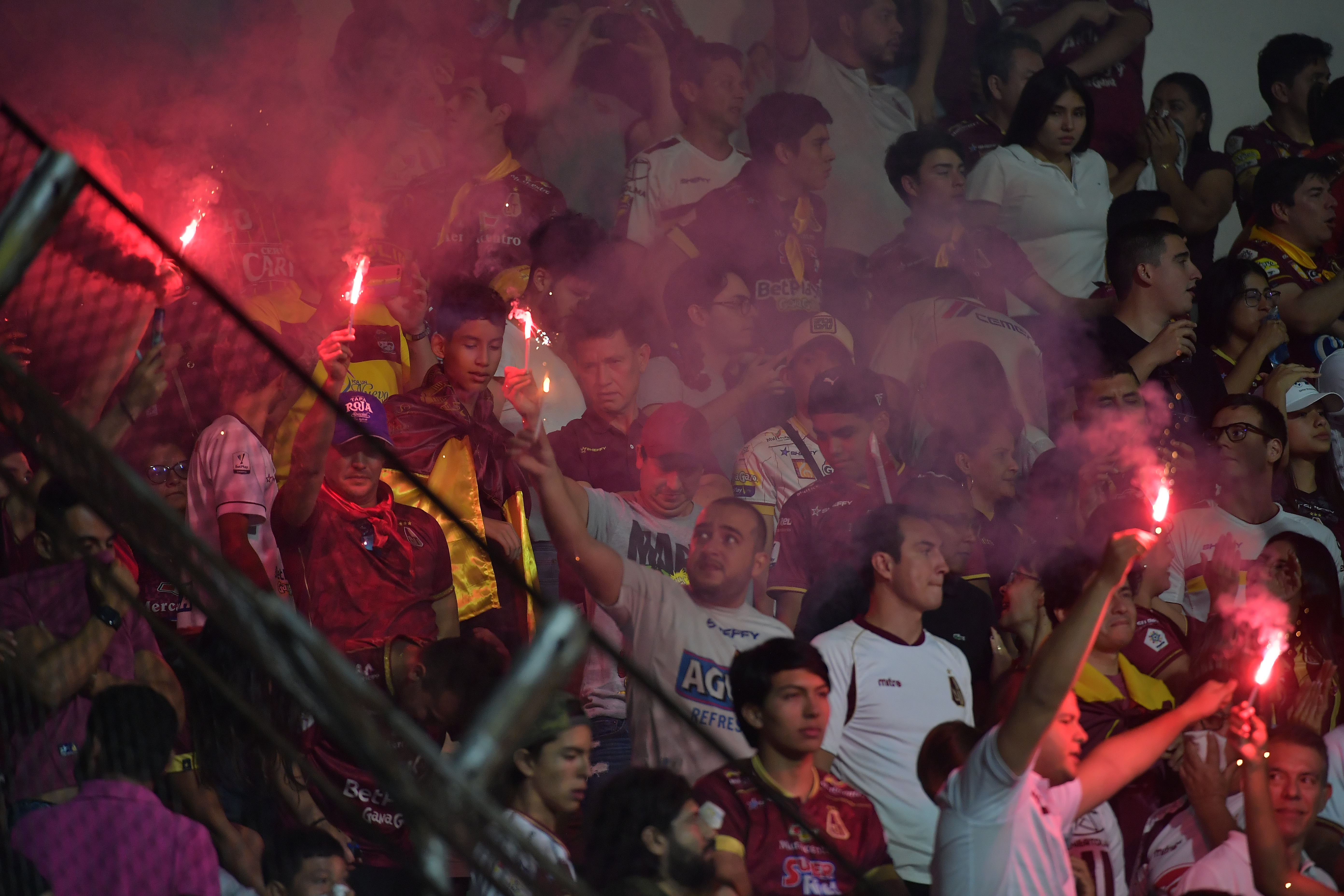 Hinchas del Tolima con bengalas y banderas en un gradería.