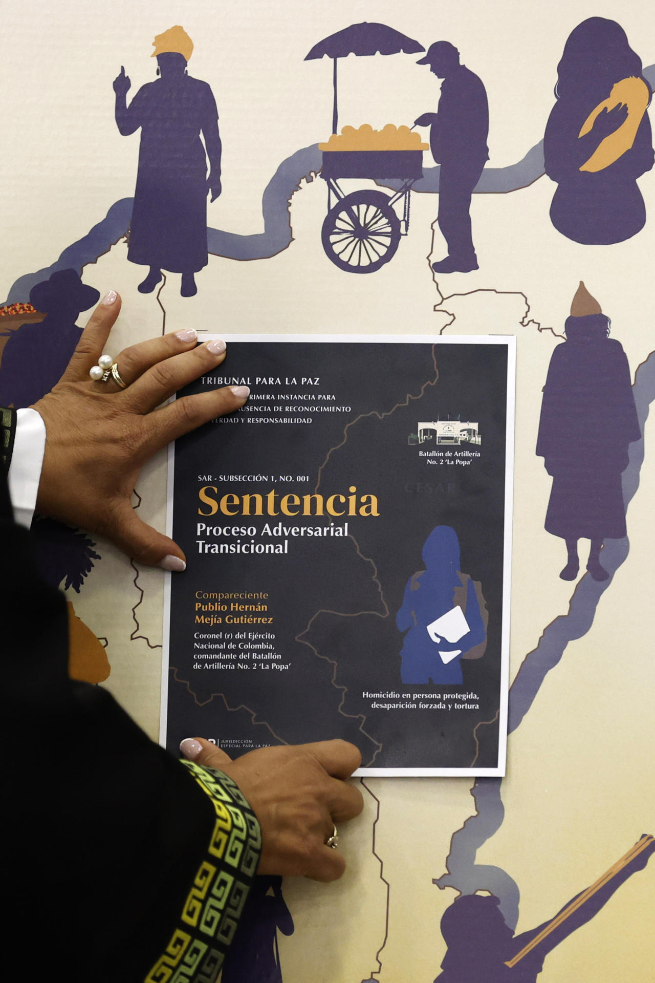 AME9578. BOGOTÁ (COLOMBIA), 19/12/2025.- La magistrada de la sección de ausencia de reconocimiento de verdad y responsabilidad de la JEP, Reinere Jaramillo Chaverra, ubica la imagen de la sentencia en un mapa donde ocurrieron los hechos violentos durante el anuncio de la Primera Sentencia Adversarial Transicional en el proceso del coronel (r) Publio Hernán Mejía Gutiérrez, este viernes en Bogotá (Colombia). La Jurisdicción Especial para la Paz (JEP) condenó a 20 años de prisión a Hernán Mejía al hallarlo penalmente responsable de crímenes de guerra y de lesa humanidad por 72 asesinatos y desapariciones forzadas de civiles presentados como bajas en combate en el norte del país. EFE/ Mauricio Dueñas Castañeda
