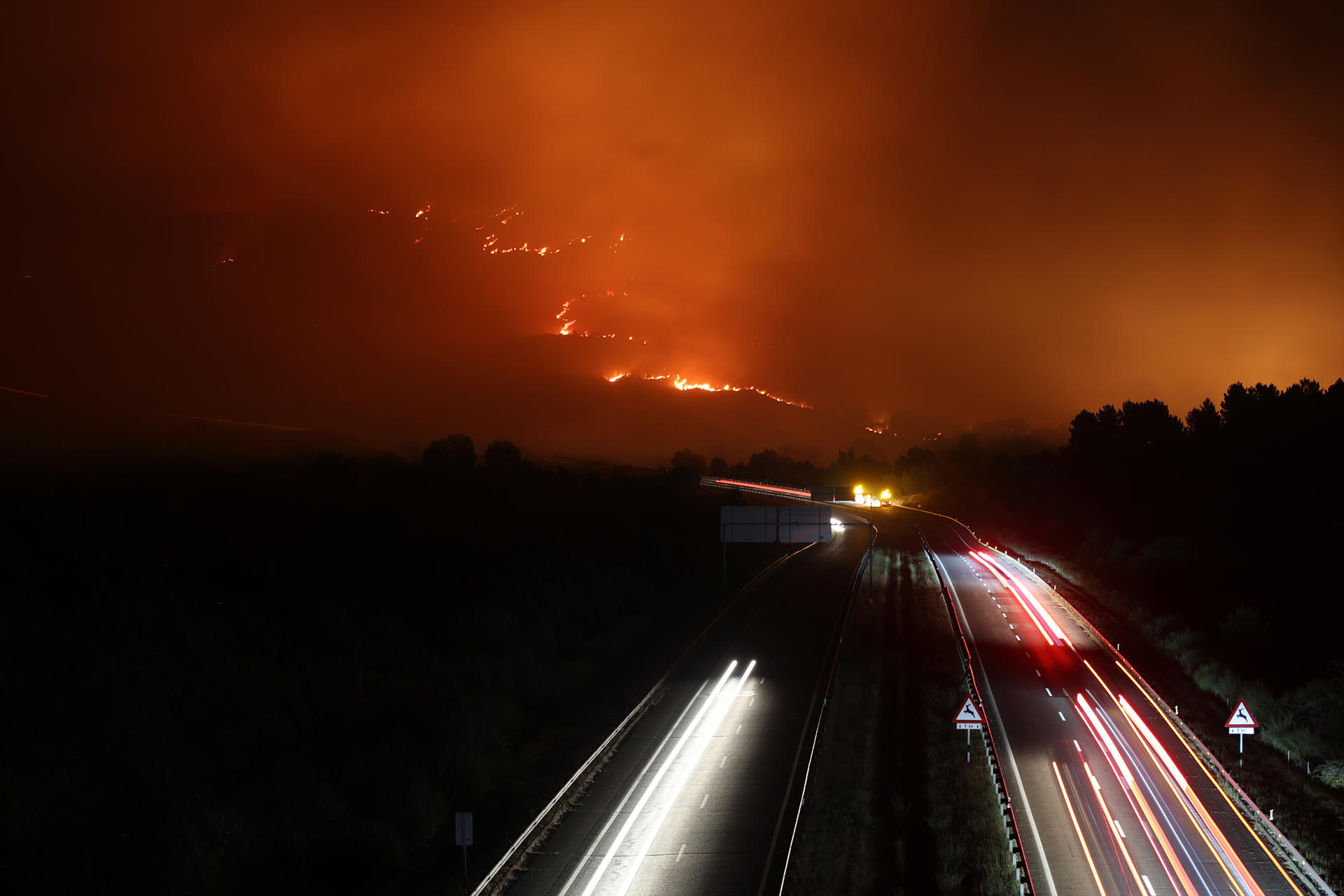 ORENSE (GALICIA), 17/08/2025.- Vista de la A-52 en la madrugada de este domingo, en Orense (Galicia) con un incendio cercano a la carretera. Trece carreteras españolas, dos de ellas nacionales, continúan cortadas en la mañana de este domingo a causa de los incendios forestales que afectan a varias provincias de Asturias, Castilla y León, Extremadura y Galicia, ha informado la Dirección General de Tráfico (DGT). EFE/ Sxenick