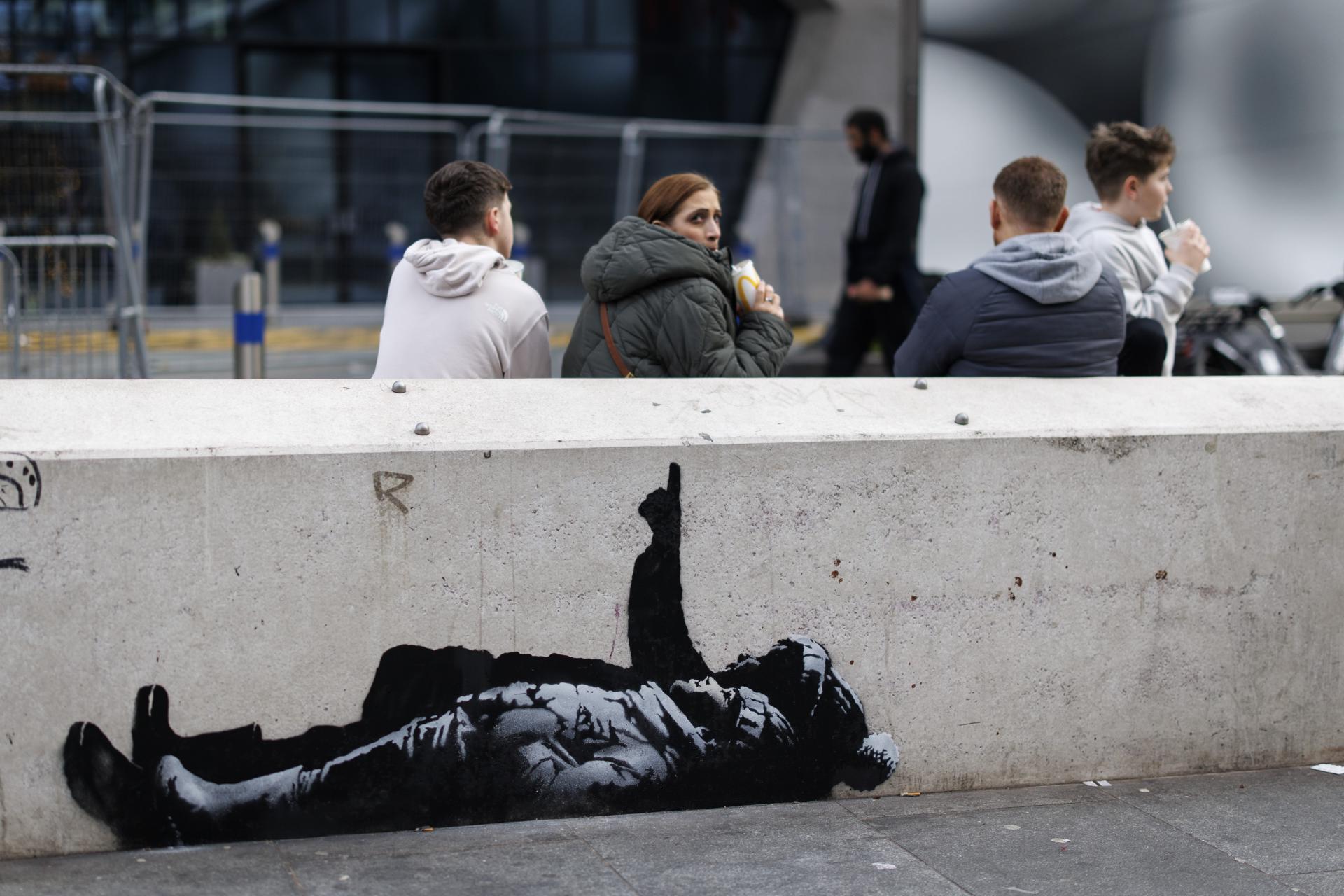 LONDON (United Kingdom), 22/12/2025.- People sit behind a new street artwork near the Centre Point building, on the intersection of Tottenham Court Road and Oxford Street, in central London, Britain, 22 December 2025. The piece has prompted speculation that British street artist Banksy may be behind the artwork. (Reino Unido, Londres) EFE/EPA/TOLGA AKMEN