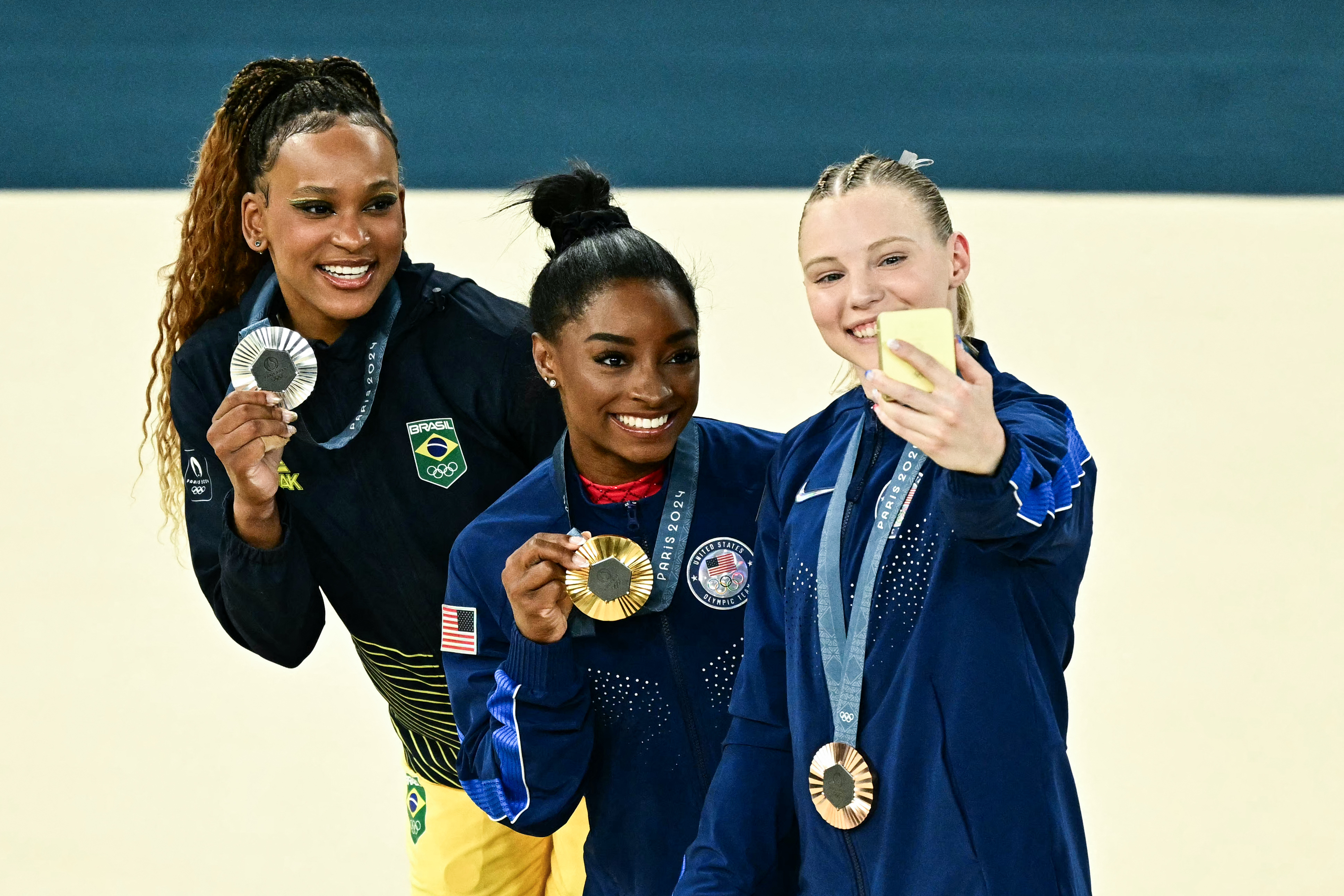 (LtoR) Brazil's Rebeca Andrade (silver), US' Simone Biles (gold) and US' Jade Carey (bronze) take a selfie during the podium ceremony for the artistic gymnastics women's vault during the Paris 2024 Olympic Games at the Bercy Arena in Paris, on August 3, 2024. (Photo by Gabriel BOUYS / AFP)